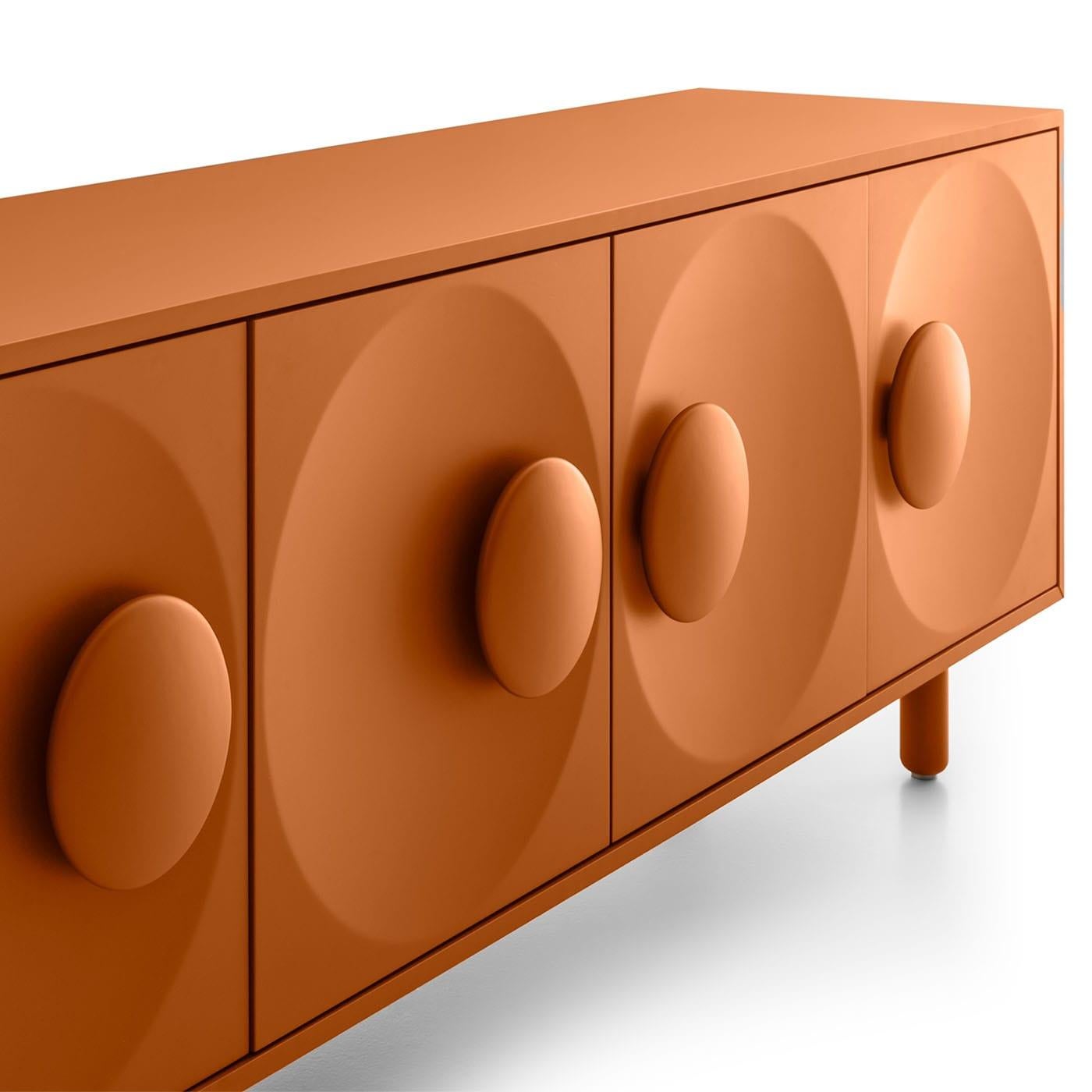 A vibrant and warm terracotta hue lends a seductive sense of authenticity to this sideboard, standing out for its button-like handles inspired by the popularity of sartorial buttons in France during the '20s. Slight concavities also characterize the