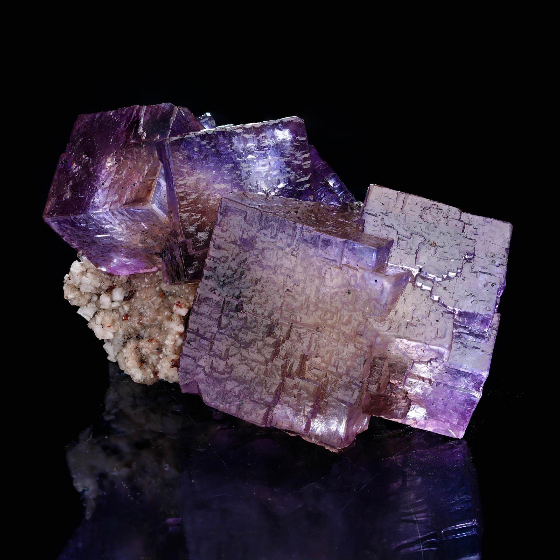 Questo raro esemplare di cristallo naturale di barite su fluorite presenta vibranti cristalli cubici di fluorite viola con una chiarezza e una suddivisione in zone eccezionali, elegantemente contrastati da una matrice di barite beige.  Poggiato su