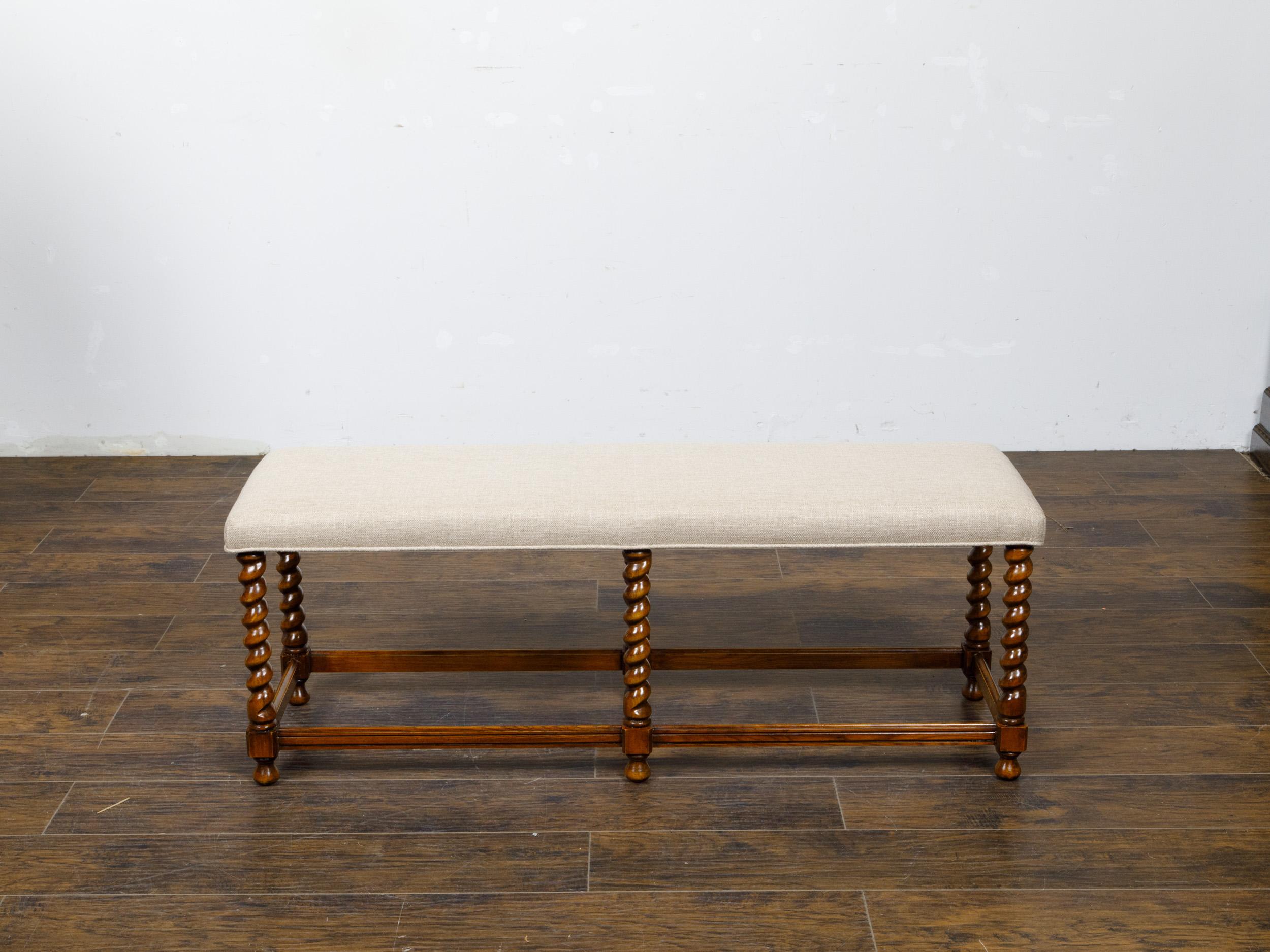 An English barley twist bench from circa 1920 with custom linen upholstery. This English barley twist bench, hailing from circa 1920, seamlessly blends traditional craftsmanship with contemporary comfort. It features a distinct barley twist base, a