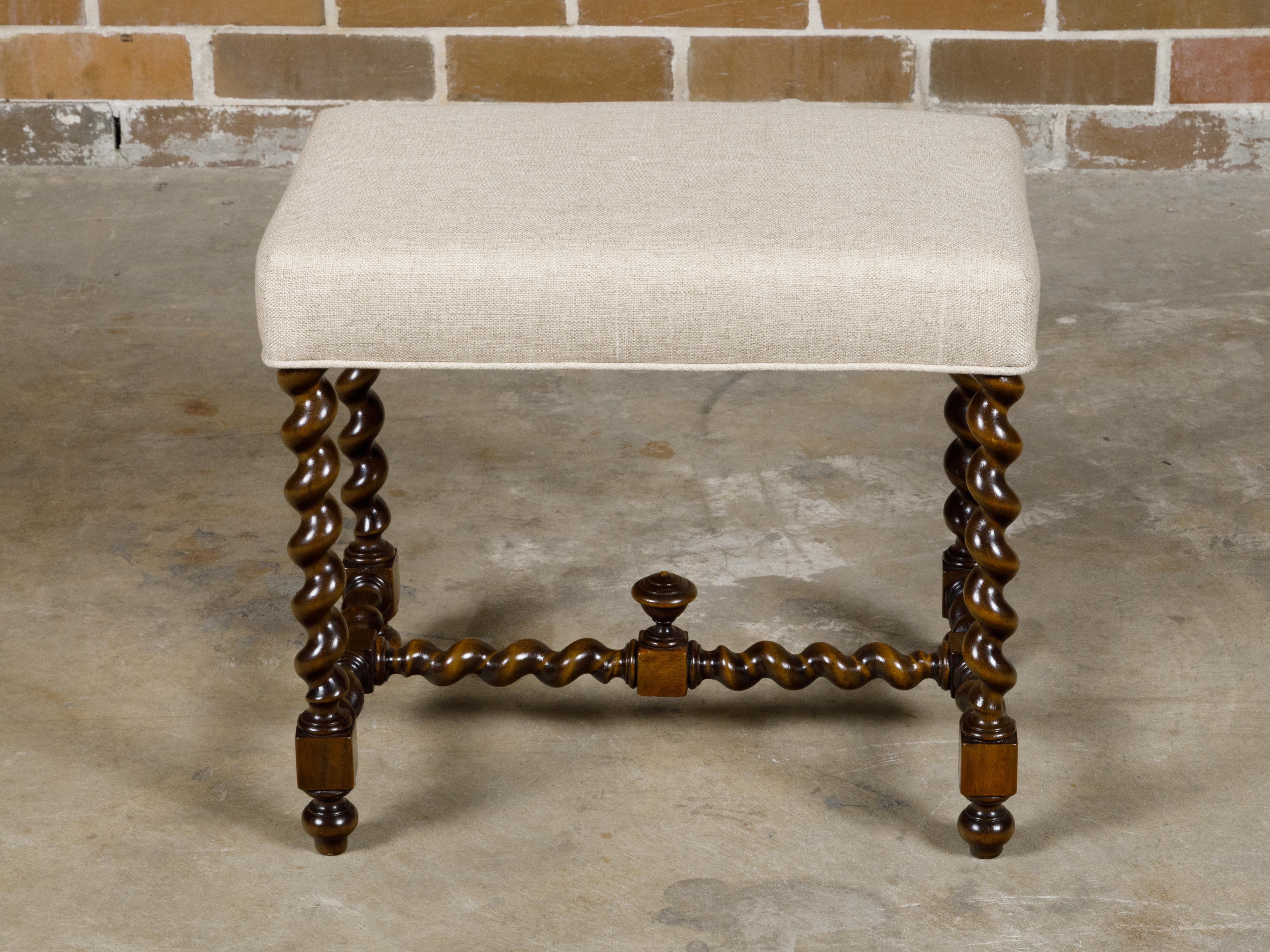 An English oak barley twist stool from the 19th century with cross stretcher and custom linen upholstery. This oak stool, featuring intricately twisted barley legs, a cross stretcher with a central finial, and custom linen upholstery, is a testament