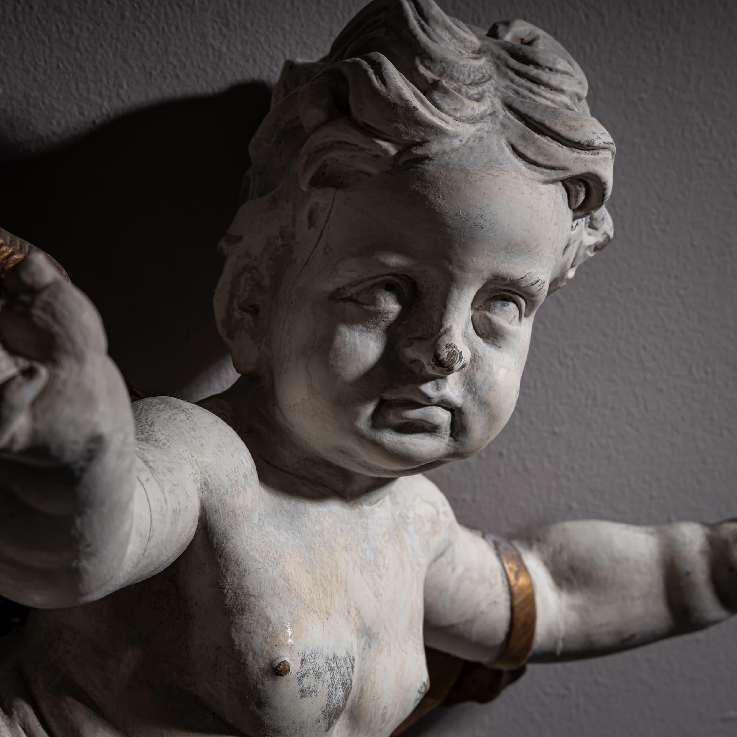 Espressiva figura di angelo barocco con un gesto ampio e capelli ondulati. Le ali, la fascia per le braccia e il perizoma sono patinati in oro, mentre il corpo è rifinito in bianco. La figura mostra il movimento dinamico tipico della scultura