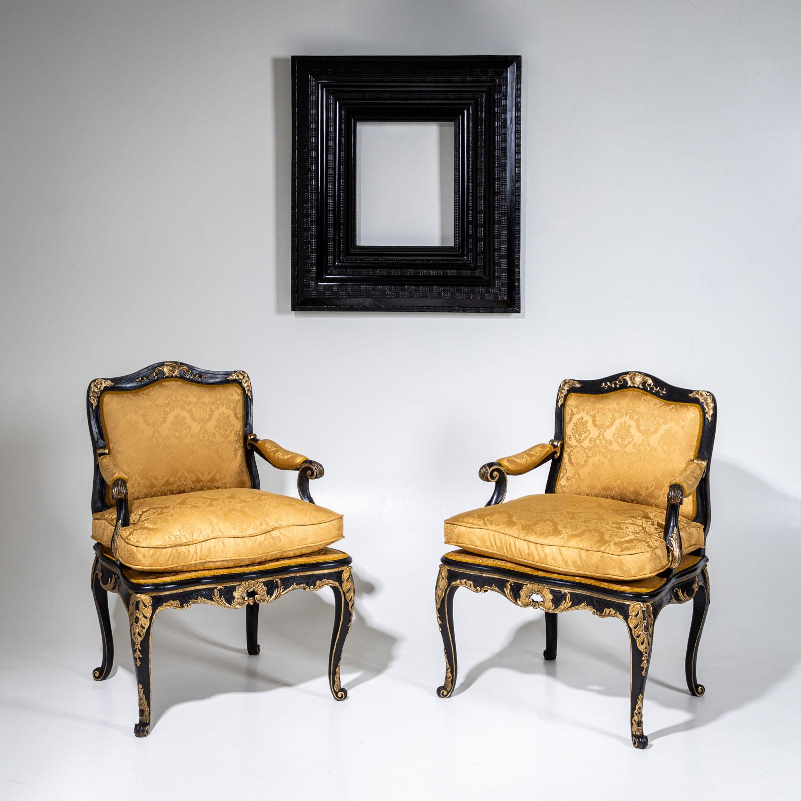 Pareja de sillones barrocos con armazón negro, con decoraciones talladas doradas en forma de conchas y rocailles. Las sillas se apoyan en elegantes patas cabriolé que se funden a la perfección con el armazón curvado. Los reposabrazos empotrados