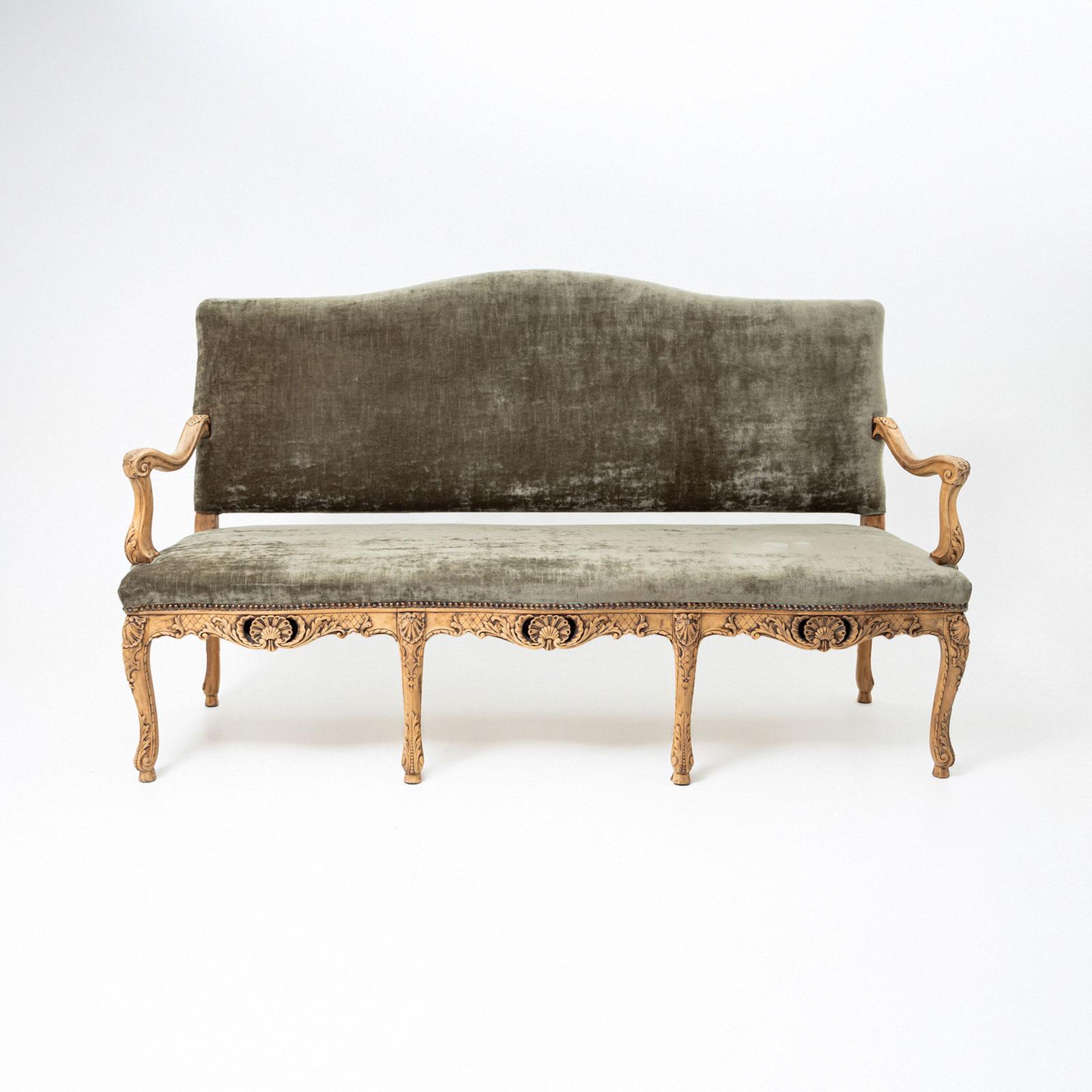 Un grand banc baroque du XVIIIe siècle, soutenu par six pieds cabriole élégamment courbés. Le tablier sculpté est minutieusement détaillé et mis en valeur par des motifs de coquillages centraux.

Les accoudoirs sont conçus en harmonie avec les