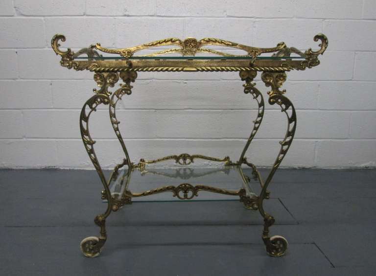 Baroque style brass two-tier bar cart with a glass top and bottom. Cart has beautiful detail. Trolley.
   