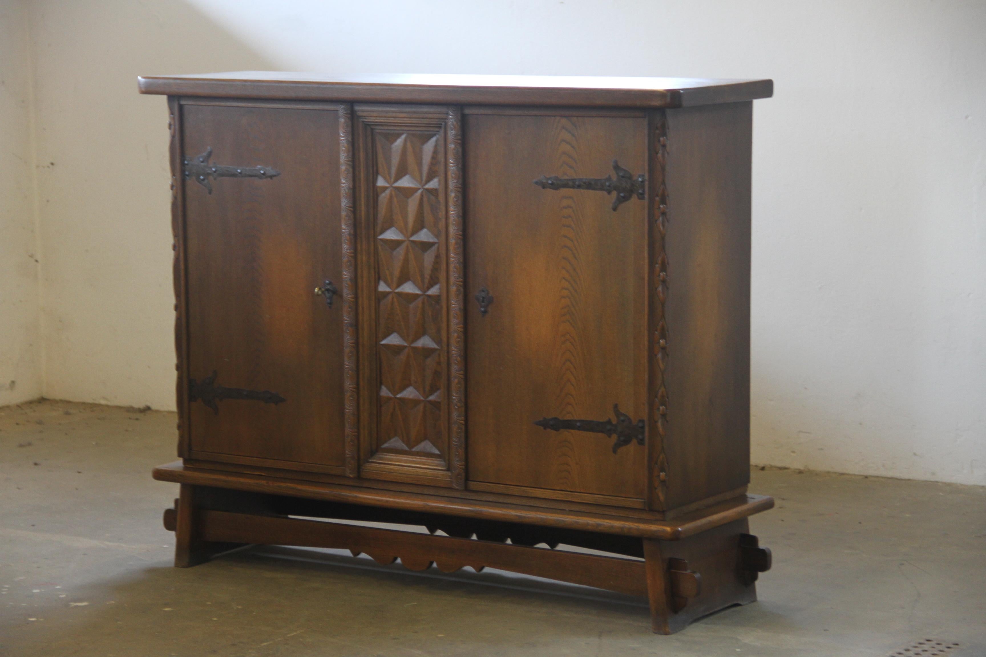This beautifully crafted cabinet is made from dark-stained oak in the style of Henning Kjærnulf, blending Baroque and Brutalist influences. Its bold, majestic presence is enhanced by intricate wood carvings and intriguing diamond-shaped patterns on