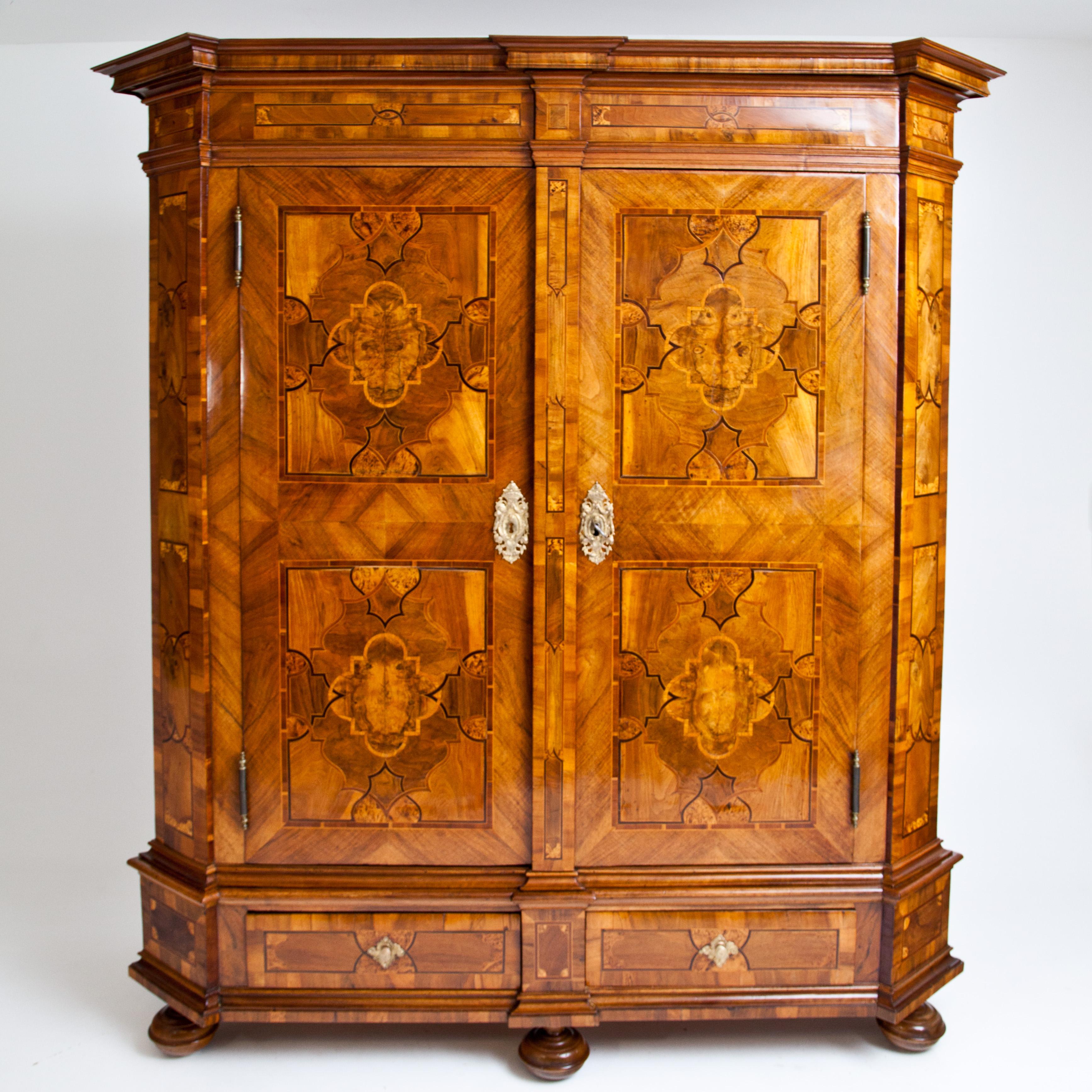 Two-door baroque cabinet on profiled bun feet with bevelled corners and pilasters. In the base are two drawers with brass pull handles, between two profiled strips. The flat cornice is also slightly cranked and set off by profiled strips. The doors