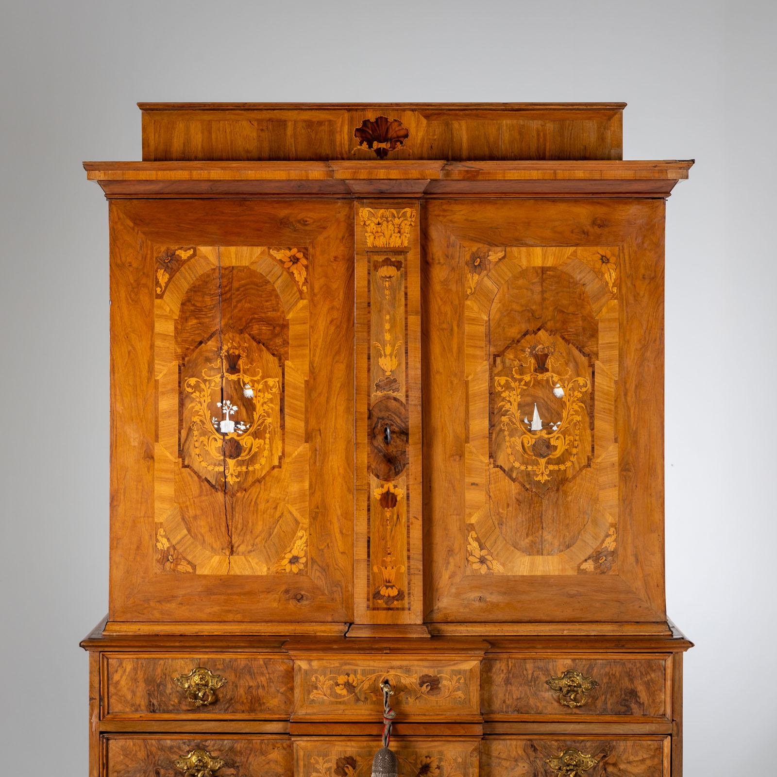 Large two-door Baroque cabinet with two wide drawers with a slightly protuding central risalit, on a six-legged stand with baluster legs and intermediate struts. The body is veneered in walnut and inlaid with leaf marquetry and decorated with bronze