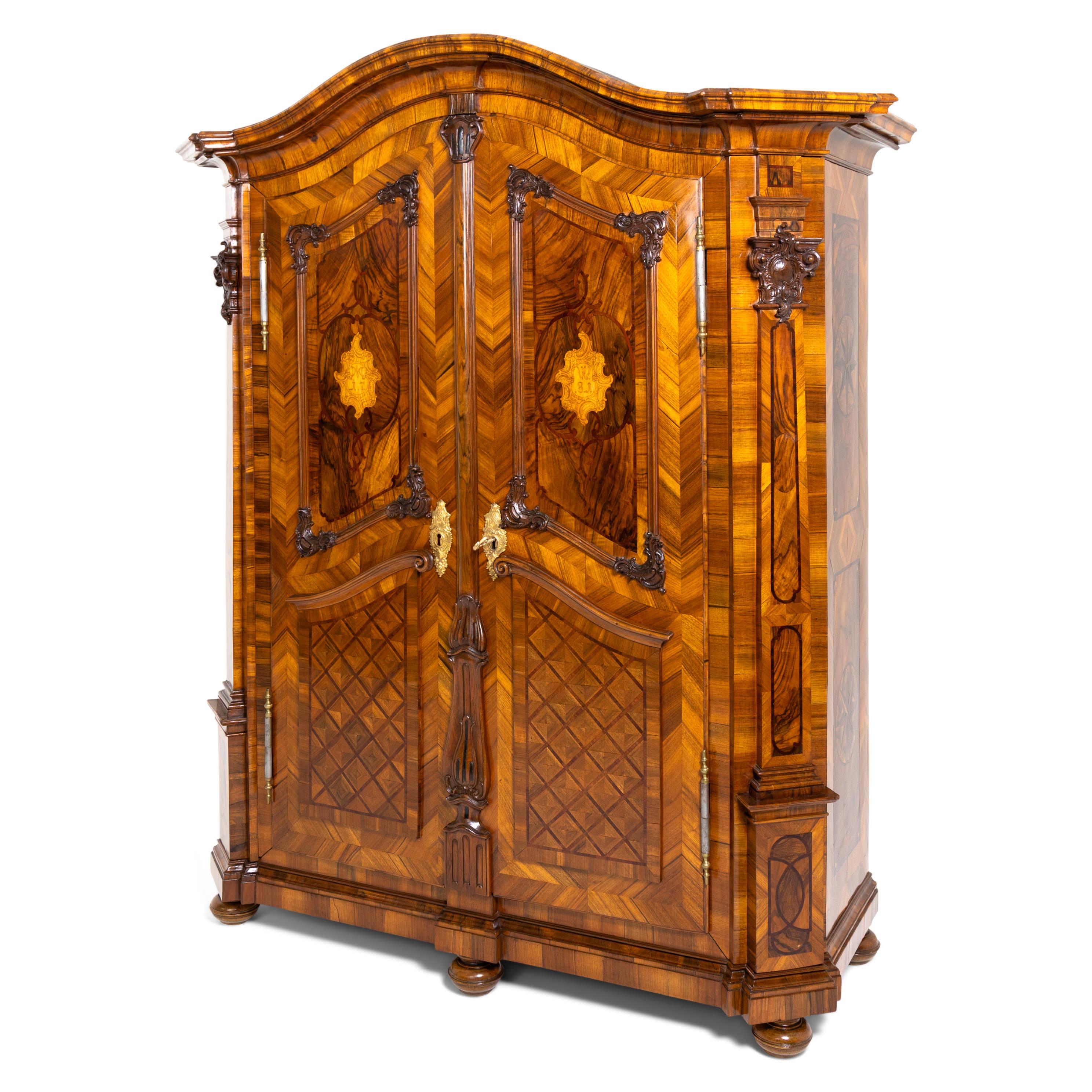 Large two-door Baroque cabinet, veneered in walnut, standing on pressed and profiled ball feet, with elaborate Rococo carving decoration and rich strap work marquetry. The cabinet is crowned by a curved, profiled pediment and flanked on the sides by