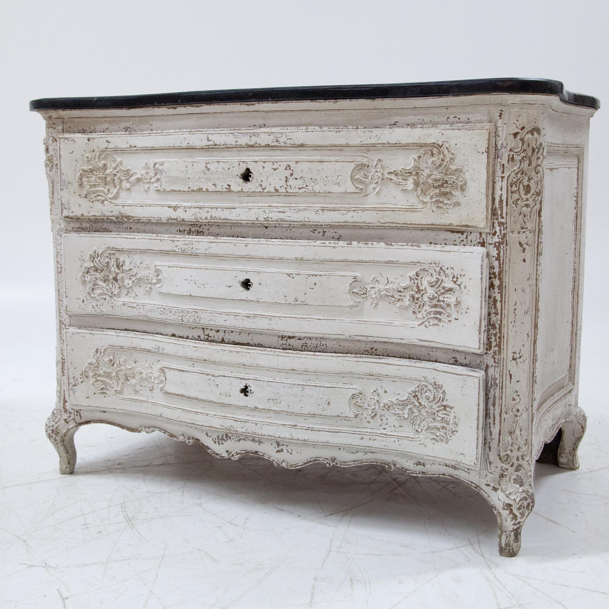 Baroque commode with a black marble top, three drawers and slightly curved front and sides standing on S-shaped feet. The sides with profiled filling panels, the fronts with floral relief carvings. The corners are also decorated with rocailles and