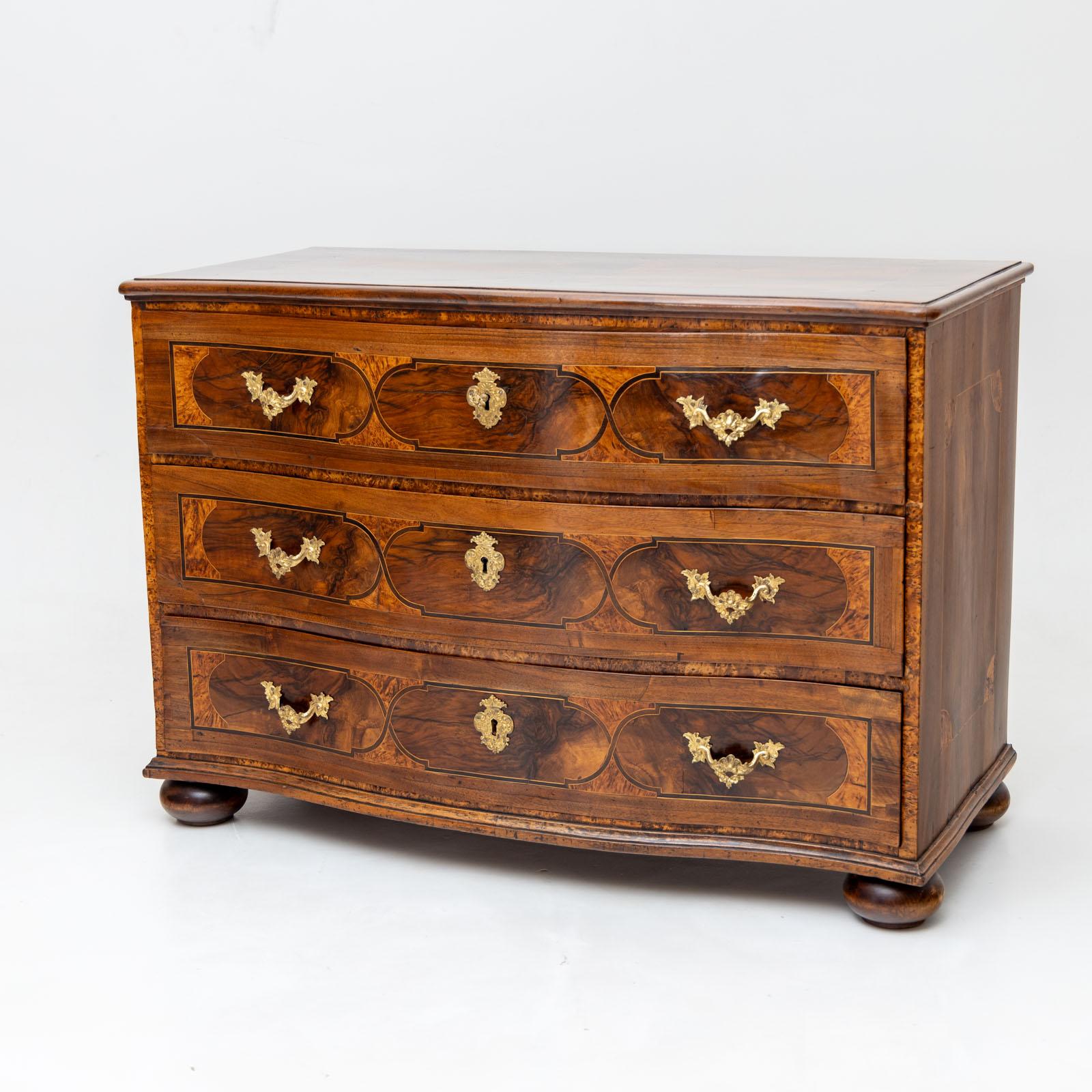 Large baroque chest of drawers with a curved front and three drawers. The chest of drawers rests on pressed ball feet and is profiled at the edges. The fronts of the drawers feature inlaid panels with framing marquetry in walnut. The sides and top