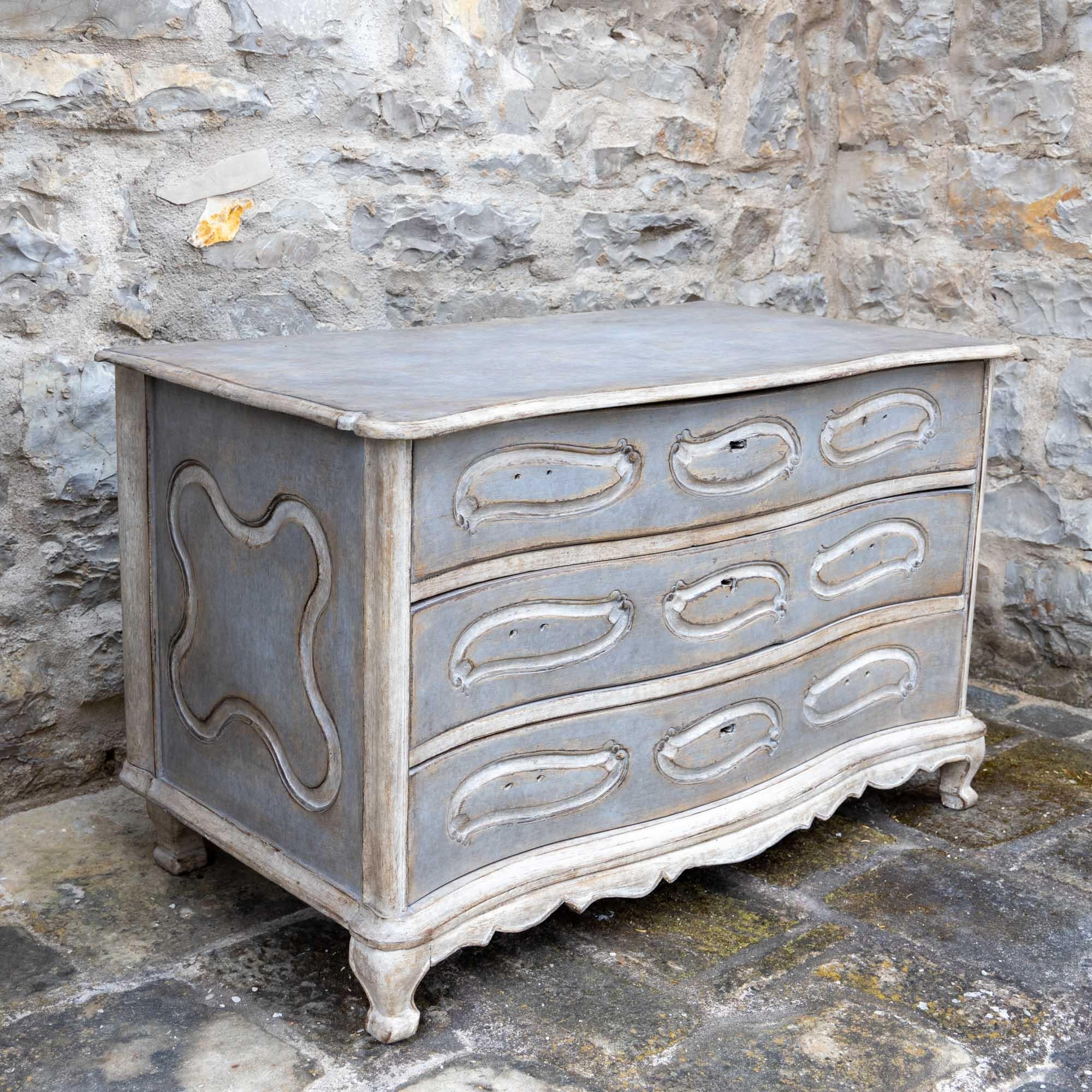 A three-drawer baroque chest of drawers with a moving panel and a curved frame. The frame in light grey and creamy white is new and has been decoratively patinated.