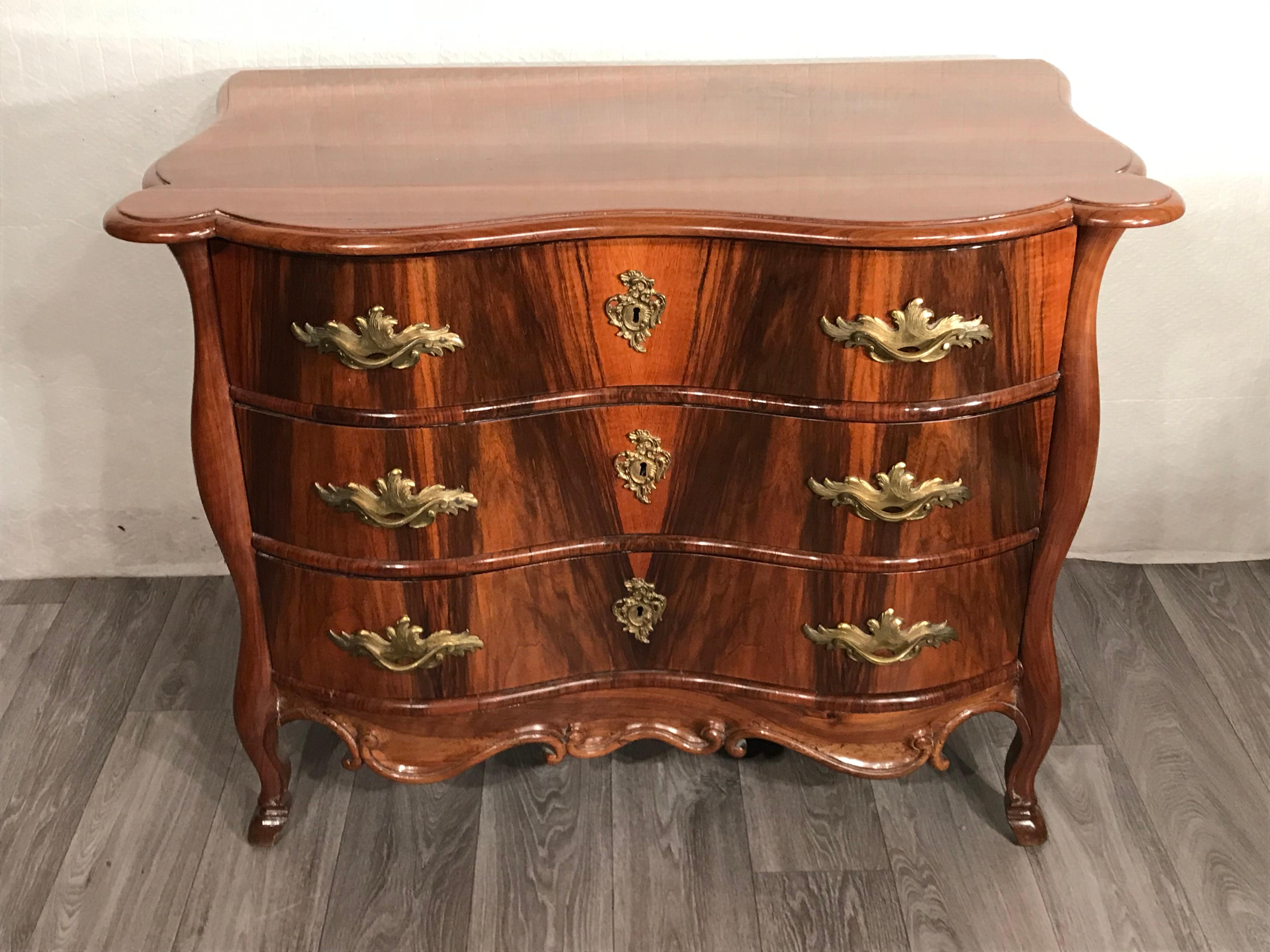 Baroque chest of drawers, Switzerland, 1750.
The 18th century three drawer commode has walnut veneered curved drawers, sides and top. The curved legs and the curved edging next to and below the drawers are made of carved walnut. The bronze fittings
