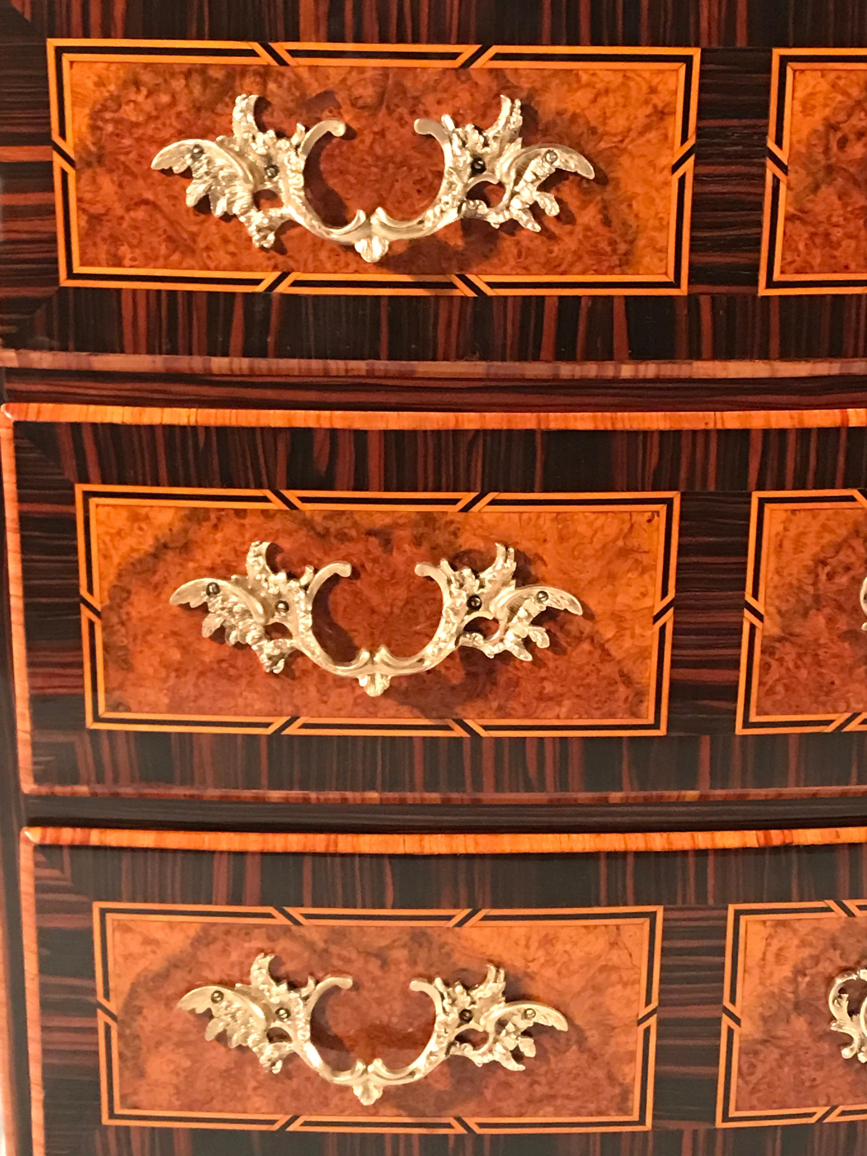 Questa cassettiera barocca unica nel suo genere è stata realizzata nel XVIII secolo in Svizzera. Il comodino a tre cassetti ha una bella impiallacciatura in legno di acero e kingwood con dettagli in palissandro su una struttura in legno di pino. La
