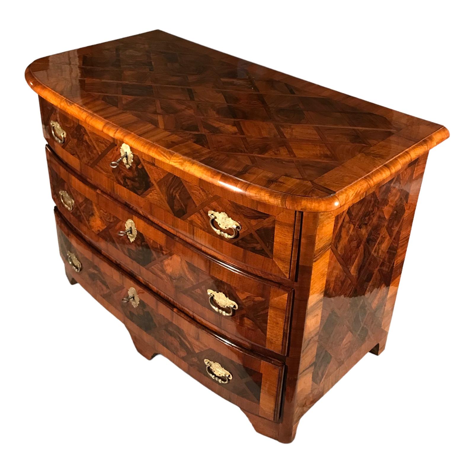 This original 18th century baroque chest of drawers comes from Switzerland. It dates back to around 1760. The three slightly convex three drawer chest has a very pretty walnut veneer pattern with diamond shaped inlays. The chest has been expertly