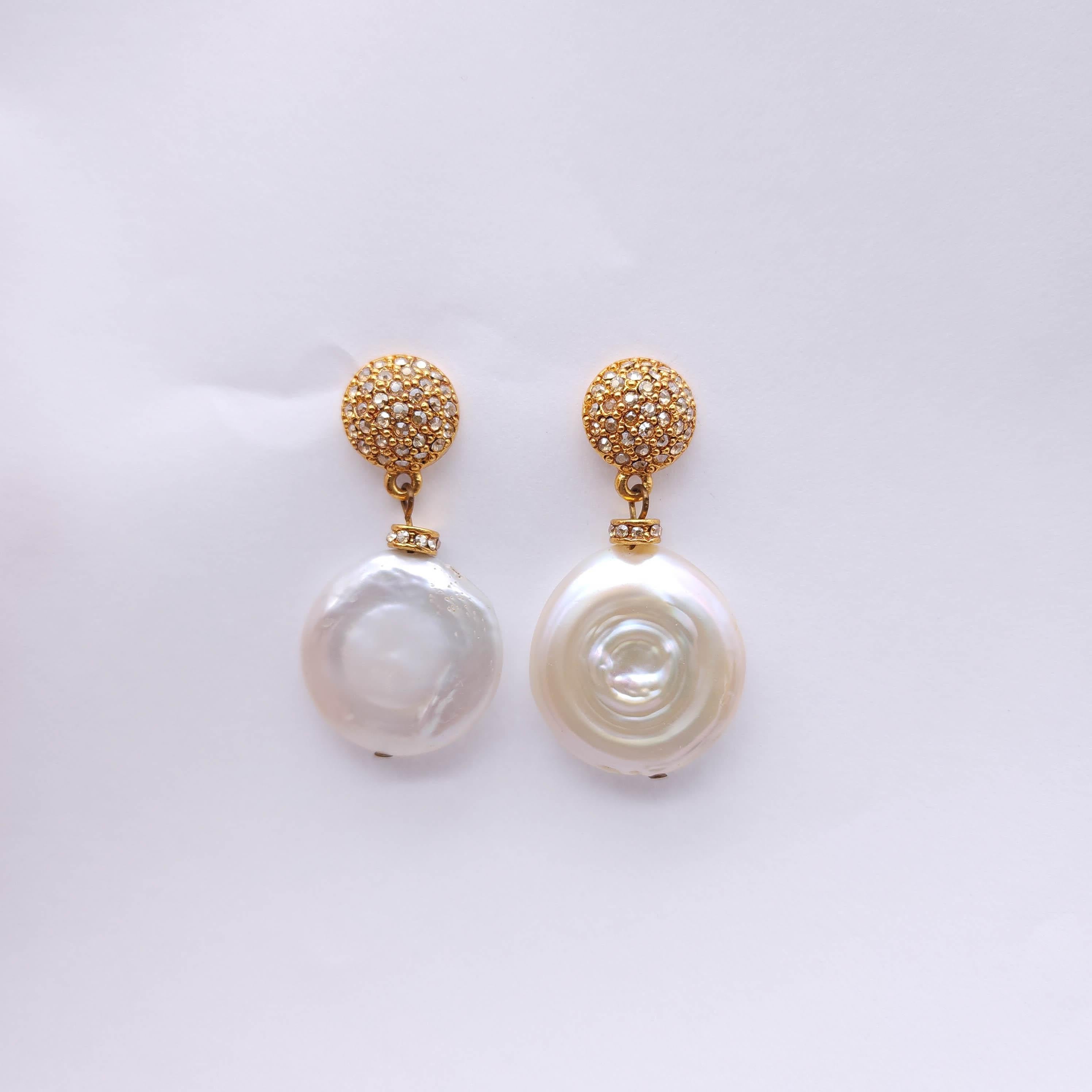 Elegantes y texturizados, estos pendientes colgantes resaltan la belleza orgánica de las perlas barrocas de imitación de monedas, combinadas con un brillo glamuroso.

Cada pendiente presenta una luminosa perla blanca de imitación de moneda con una