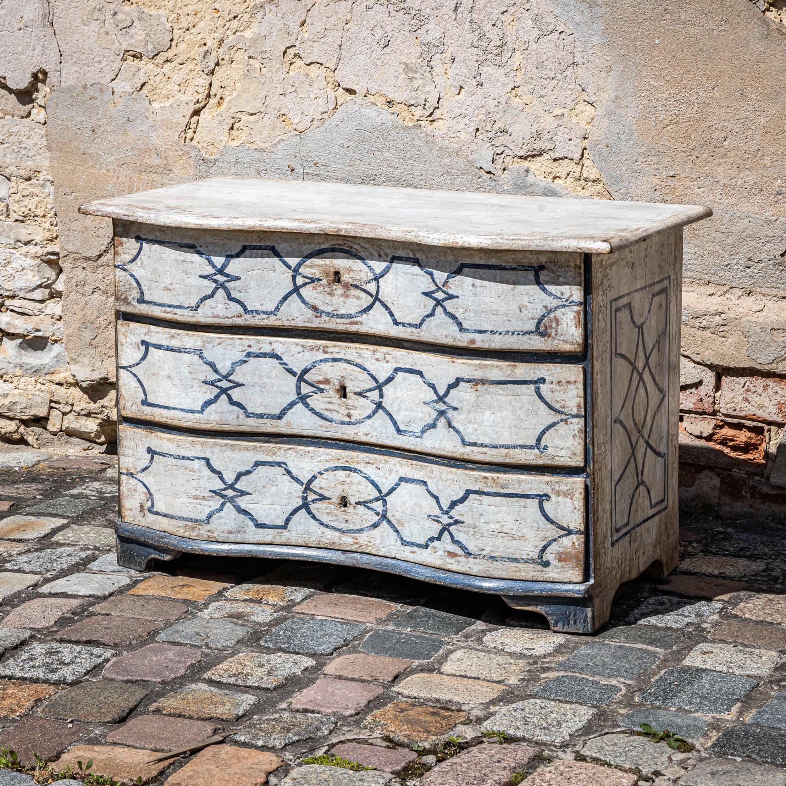 Large Baroque commode with three drawers and a serpentine front. Recently painted in the French provincial style, it features a cream white and anthracite gray color scheme with ornamentation inspired by ribbonwork motifs. The surface has been