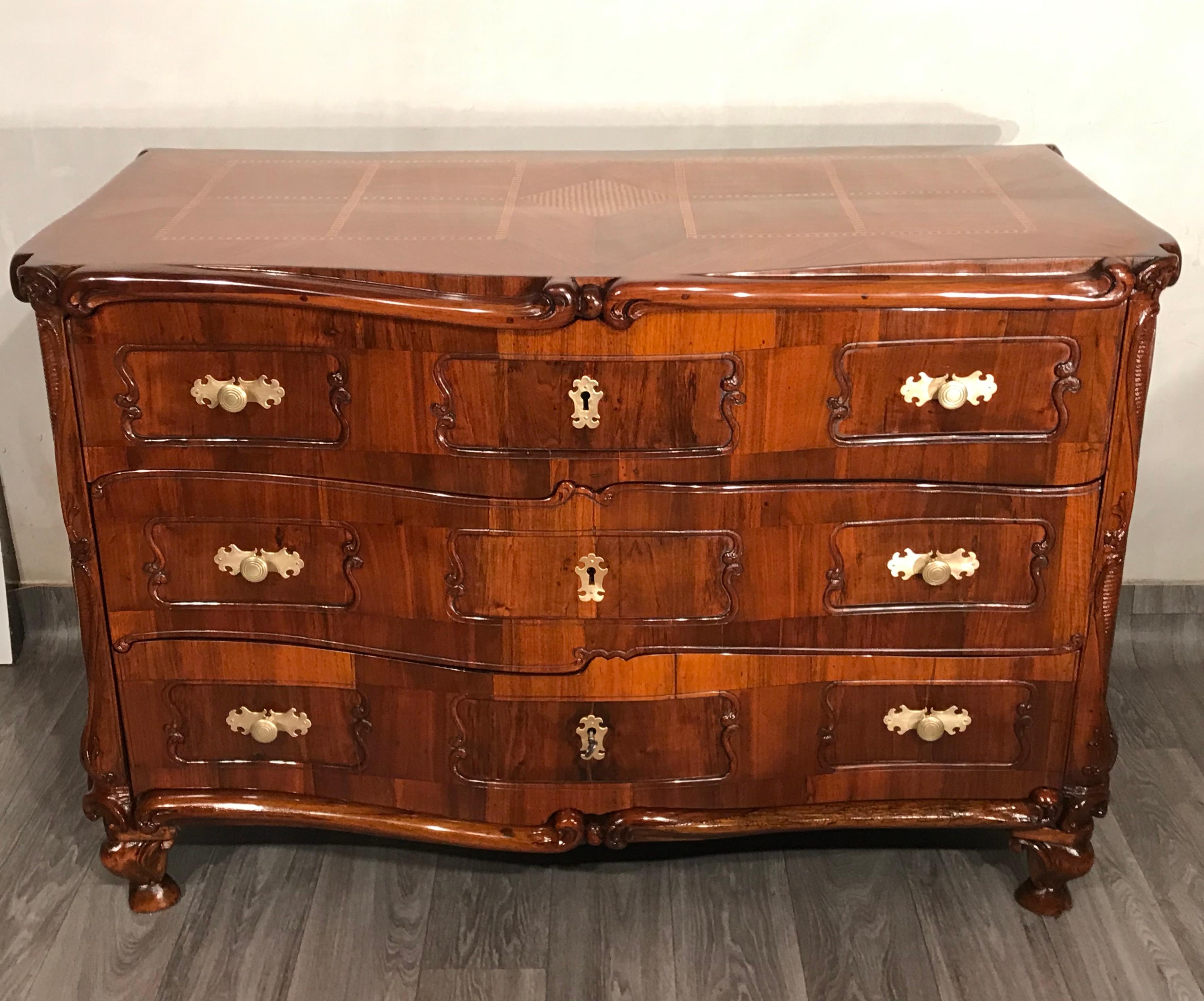 Cómoda barroca, Suiza, siglo XVIII. Esta singular cómoda barroca data de hacia 1750-1760 y procede de Suiza. La cómoda de tres cajones está adornada con chapa de nogal y decoraciones adicionales talladas a mano en el frente, los laterales y los