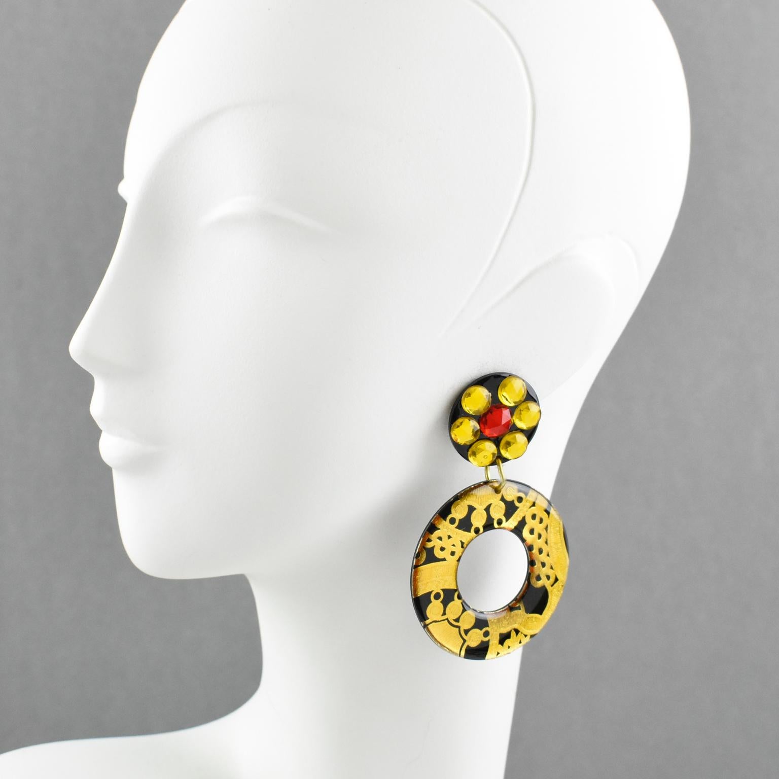 Incredible Italian Lucite dangling clip-on earrings. They feature an oversized donut shape with a baroque design in black and gold colors. The earrings are also ornate with saffron and red crystal rhinestones. 
This is a total eye-catching Pop Art