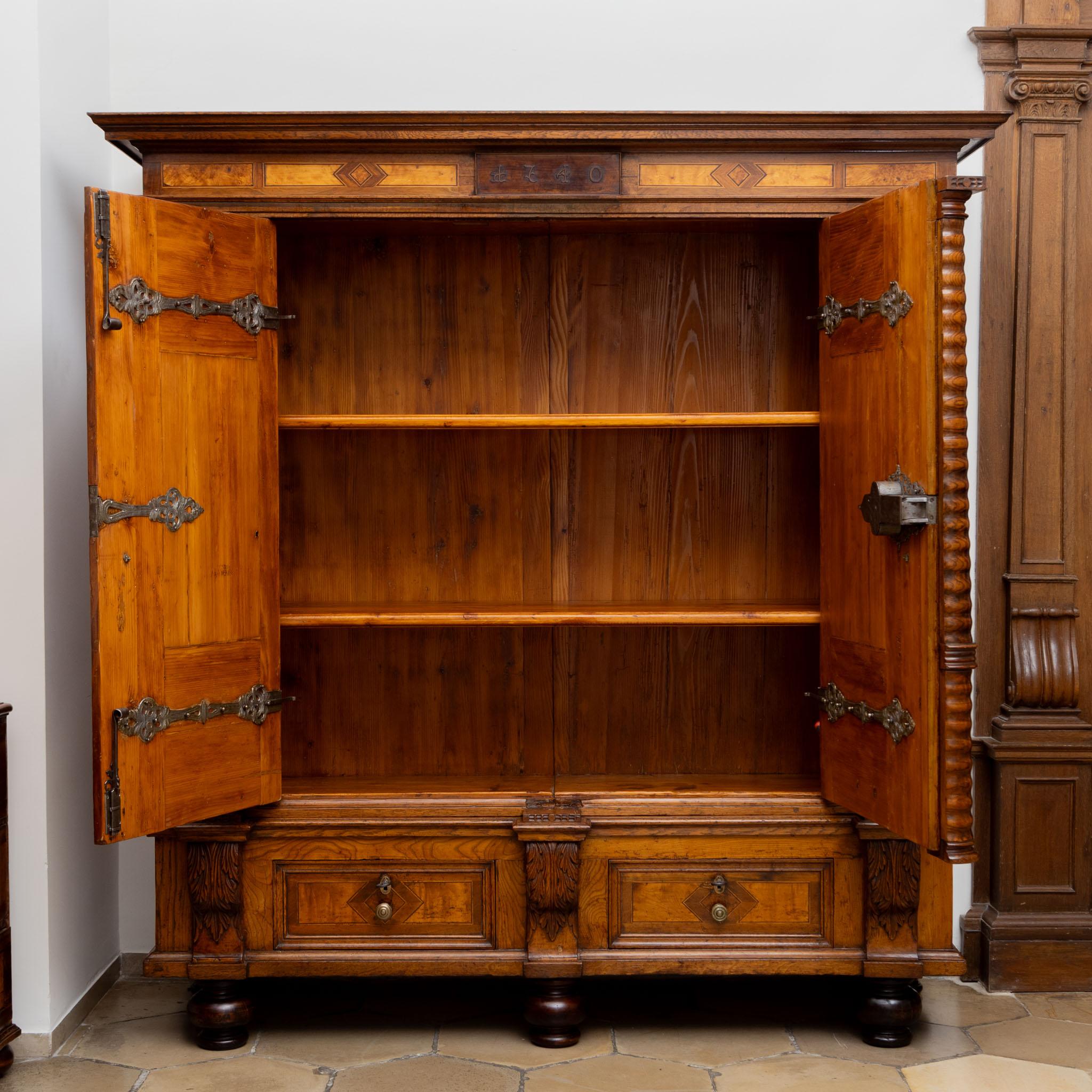 Grande mobile barocco a due ante su gambe a balaustro, con due cassetti nella parte alta della base. La facciata è strutturata da tre semicolonne ondulate e presenta nicchie architettoniche sulle porte. Queste nicchie sono ornate da colonne
