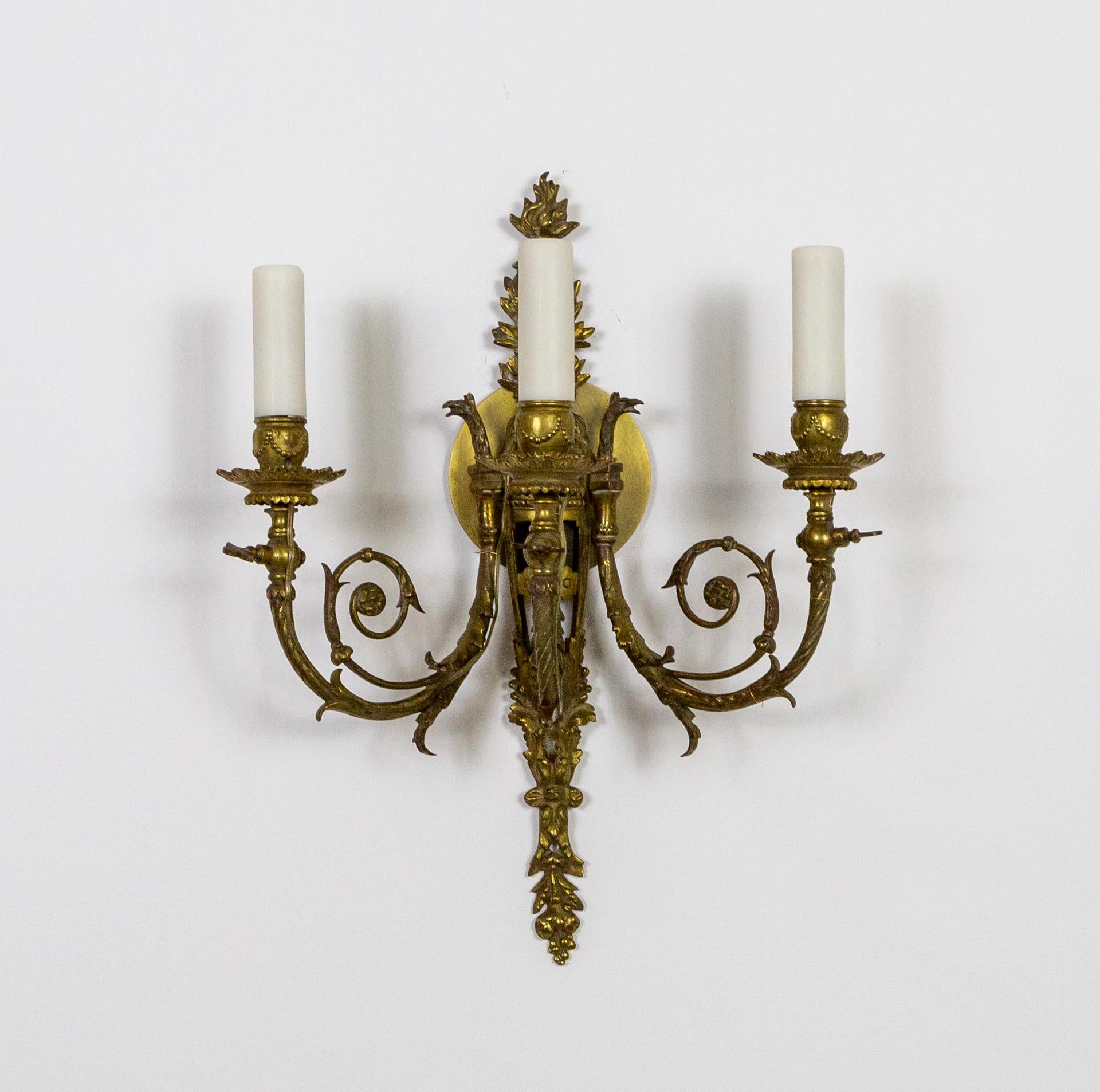 A pair of ornate, French, highly detailed, Baroque style wall sconces cast in heavy, solid brass. With delicate, fern-like curls, leaves and berries, acanthus leaves, and flame top. Three Griffin heads lead into the three swooping arms from the