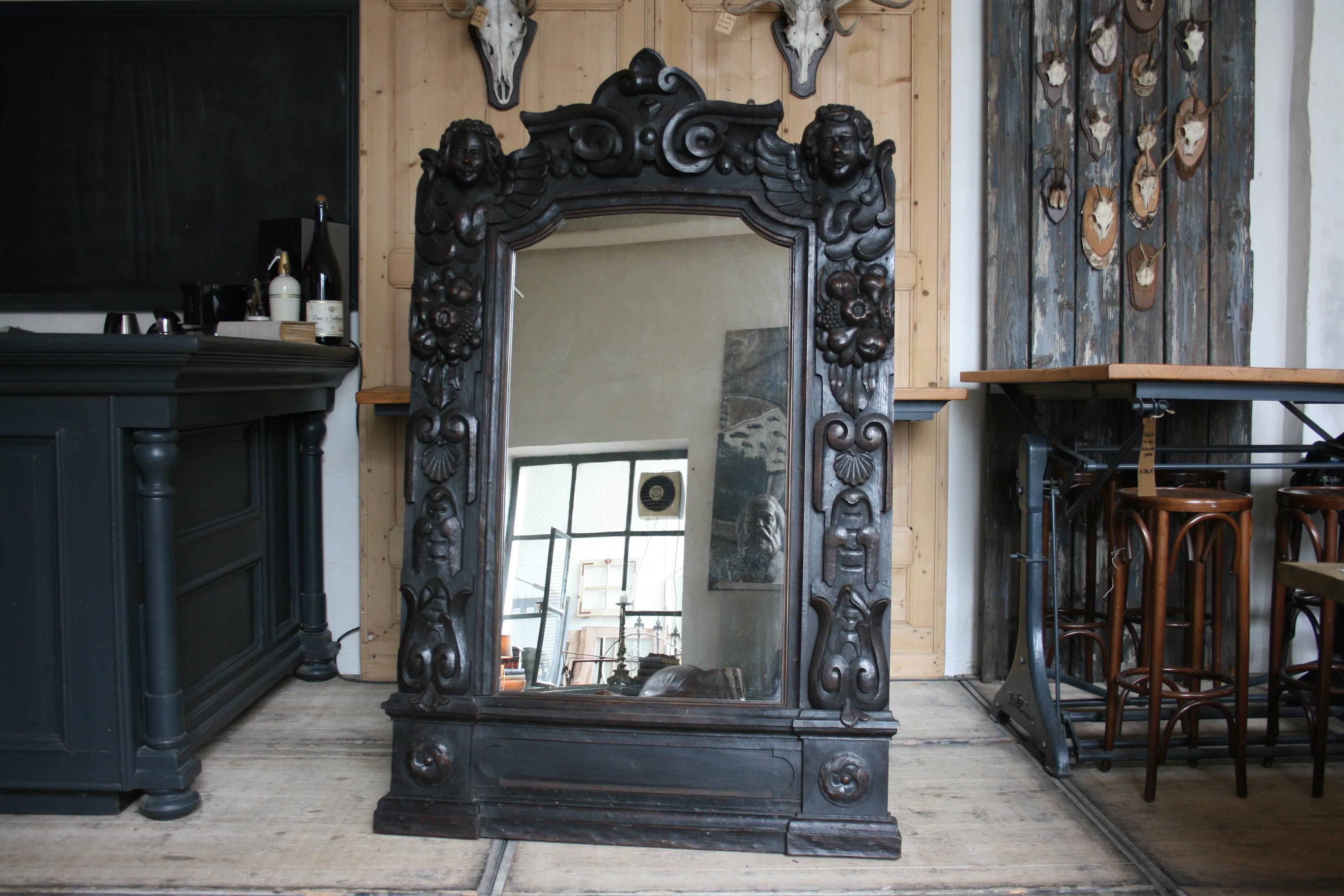 Antique Baroque mirror frame in solid oak with carving. Putti heads on both sides. New mirror inserted (probably replaced about 40/50 years ago). Mirror was originally hung over the fireplace. Can also be set free (see pictures). 
The mirror