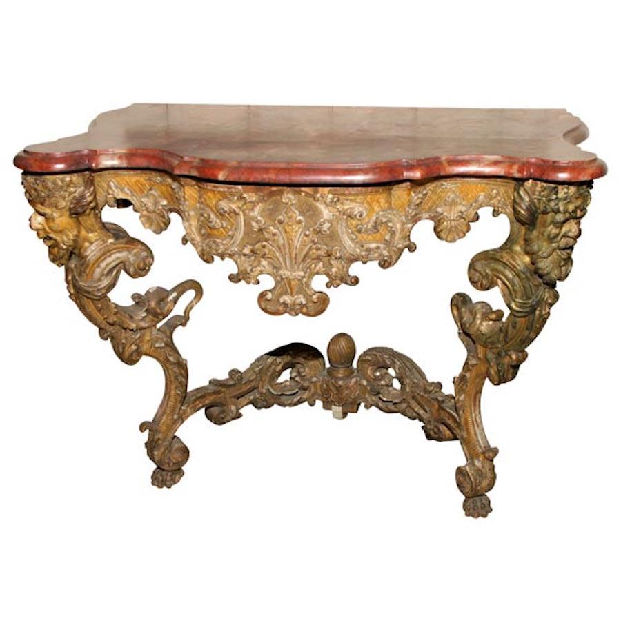 A German Baroque period giltwood console with associated shaped faux marble top supported by satyrs' masks above bold foliate scroll legs, flanking an apron carved with rocaille decoration, the in-curved stretcher carved on both sides, with paw