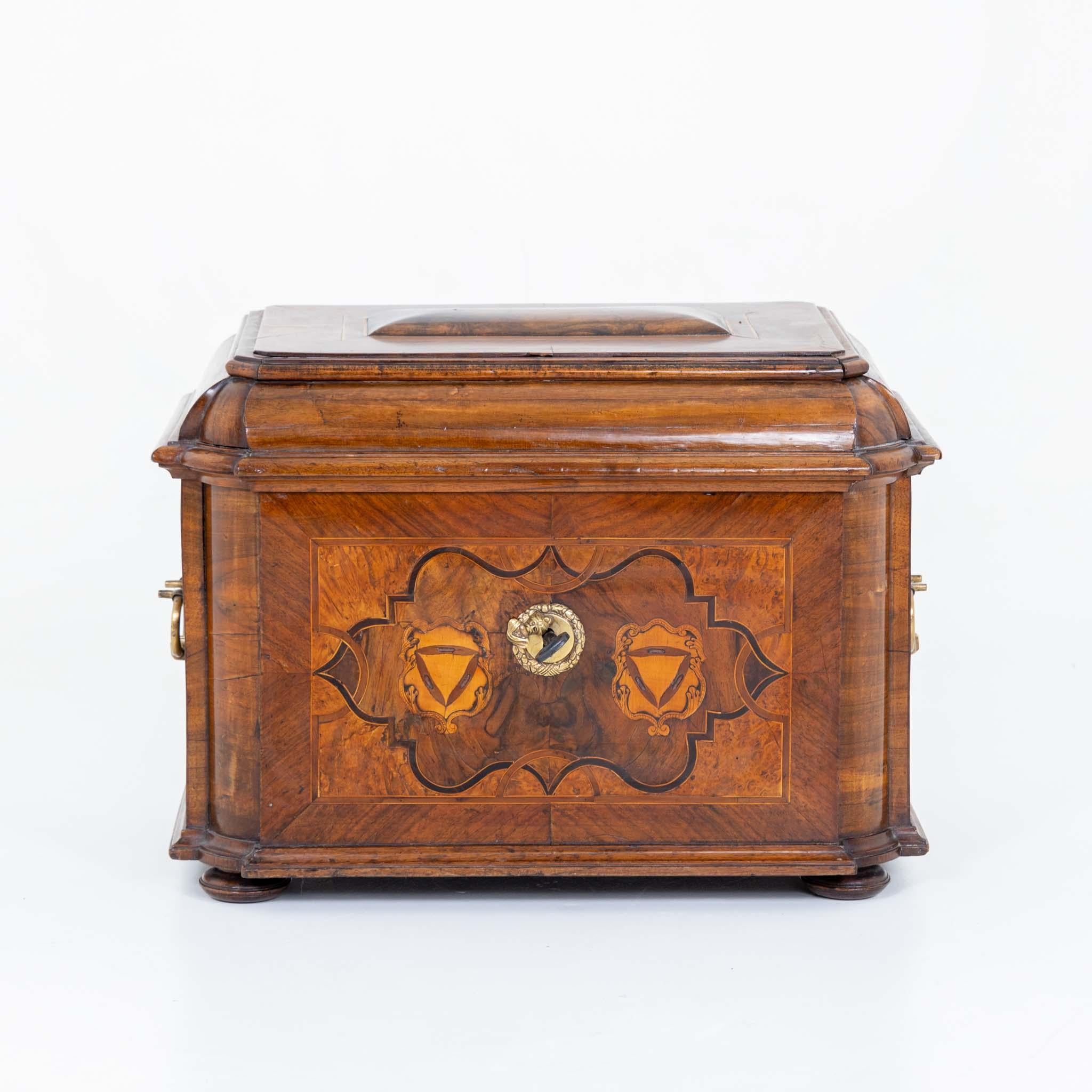 Baroque guild drawer with side brass handles and domed lid. The body stands on pressed ball feet, has rounded corners and is veneered on all sides in walnut with strapwork marquetry.