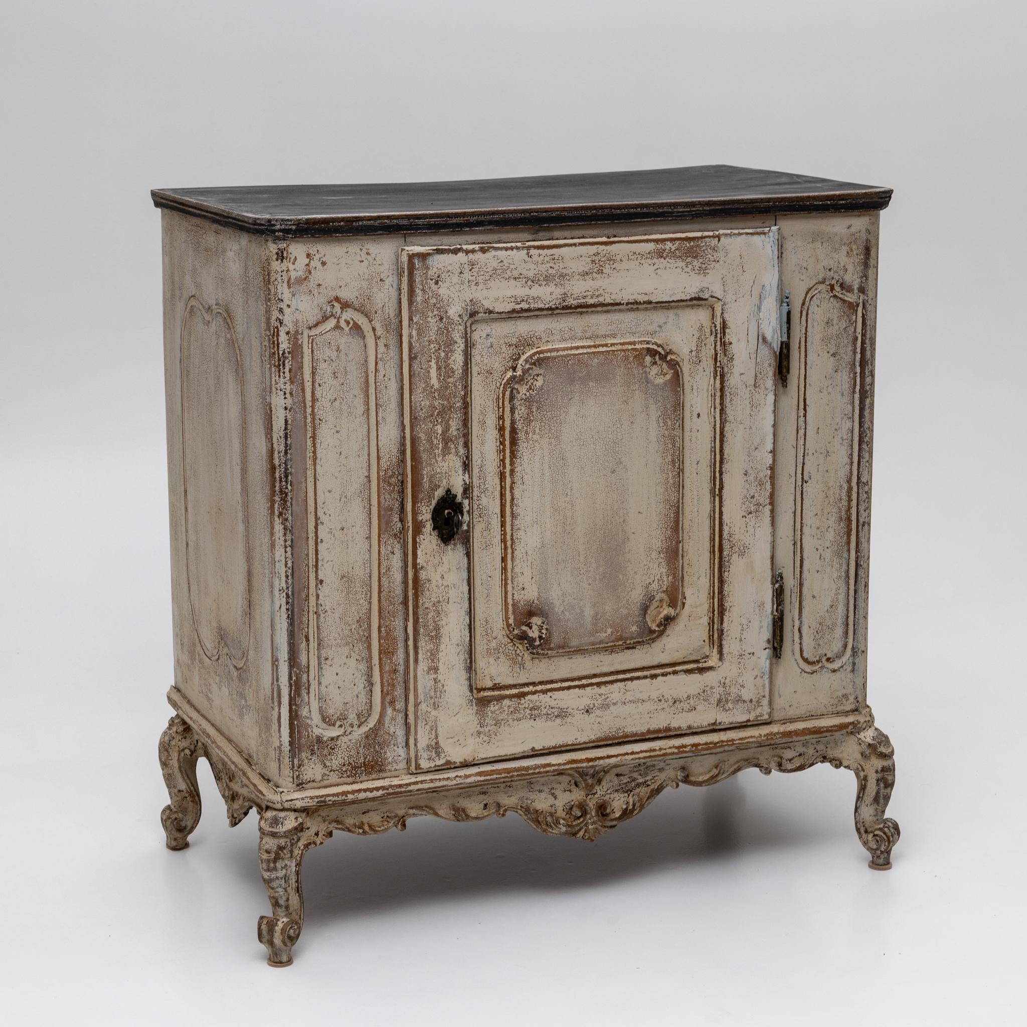 Eintüriger Barock-Halbschrank mit serpentinenförmig geschnitzter Schürze und mit Volutenmotiven verzierten Beinen. Die Karosserie ist mit dynamisch geformten, profilierten Paneelen verziert. Die cremeweiße Lackierung mit einer anthrazitfarbenen