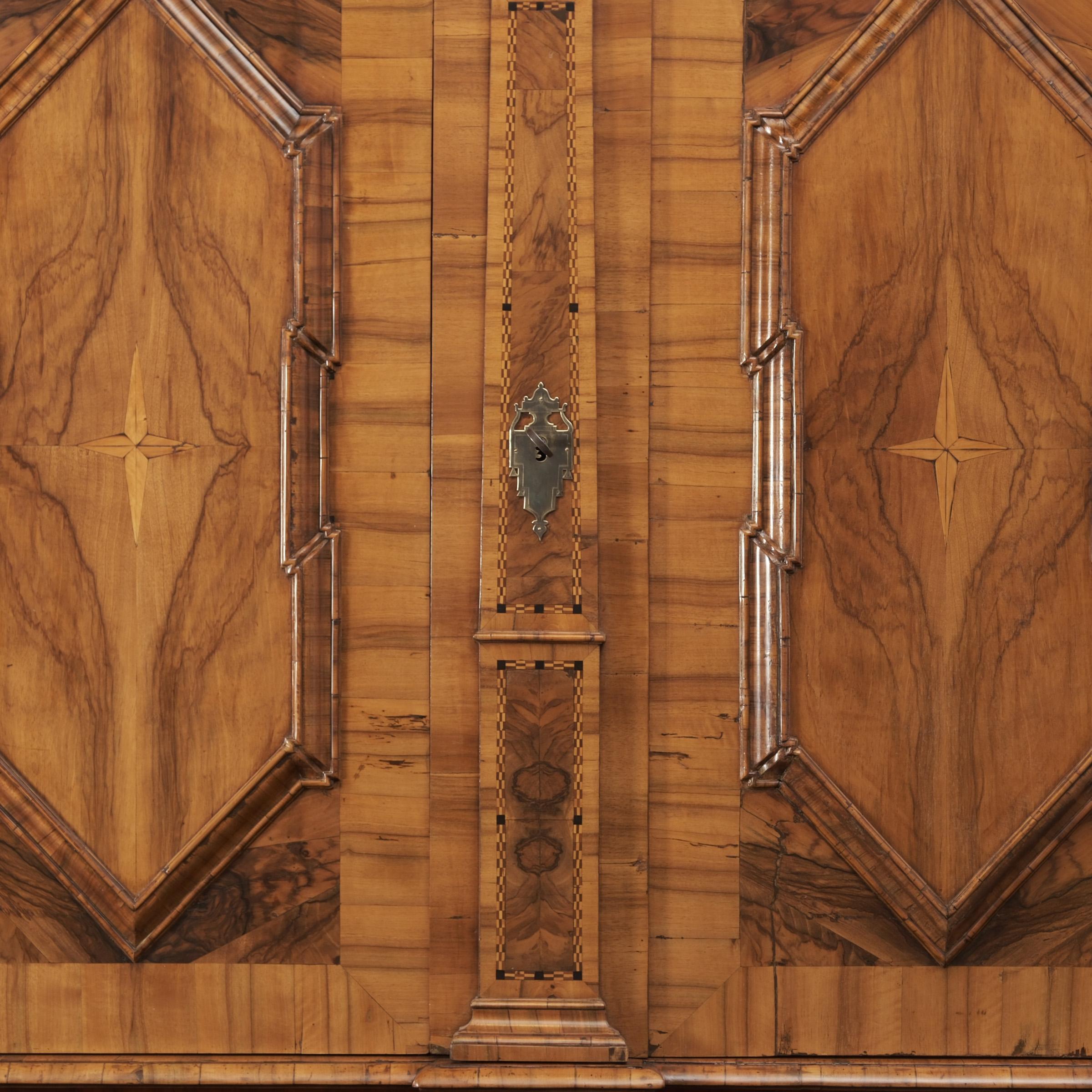
Important hall cabinet from around 1770/1780

Walnut, walnut burl and other precious woods veneered on softwood, two-door body divided by three pilasters, doors with octagonal cartouches and star inlays, geometric ribbon inlays, overhanging cornice