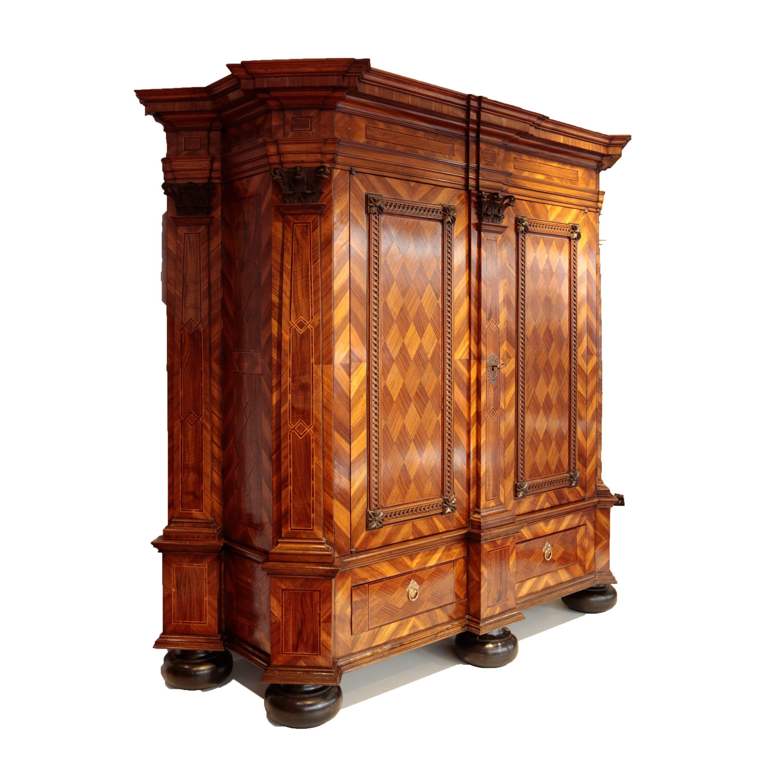 

Armario de salón de los ebanistas Budde Warendorf, Westfalia, hacia 1770, chapado de nogal y ciruelo sobre roble, elaborado motivo de chapado geométrico, decoración en bandas, cuerpo prismático con cornisa escalonada, cinco pilastras con capiteles