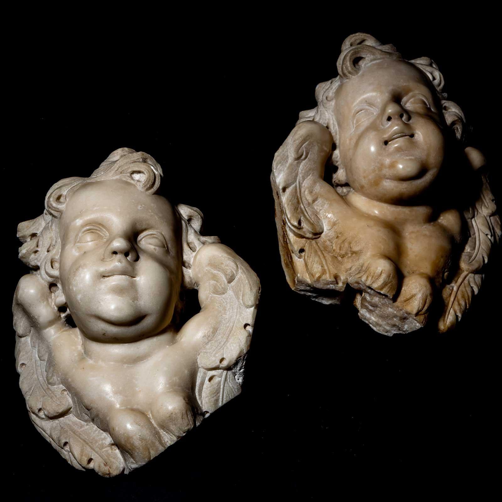 Two marble angel heads with curly hair and hints of wings, designed in the opposite style.