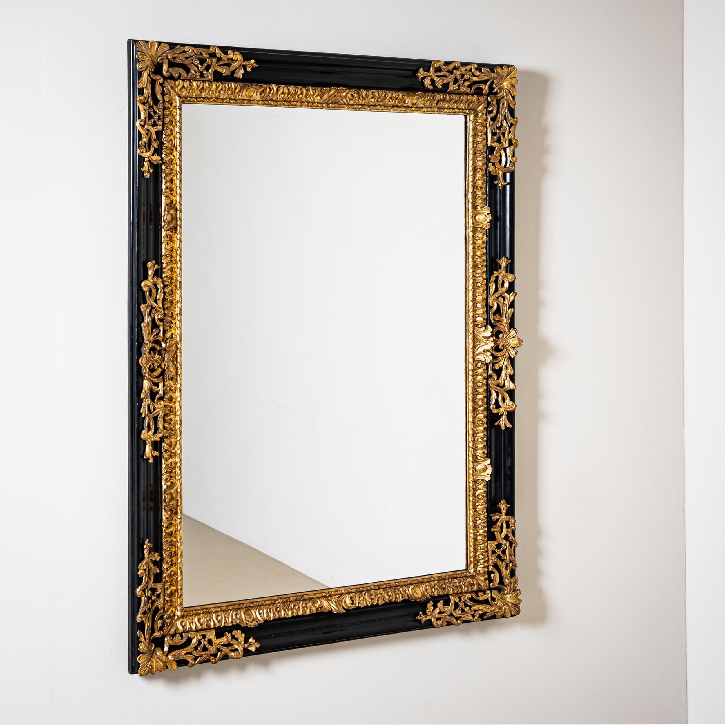 A grand Baroque mirror from the first half of the 18th century. The frame features a black lacquered exterior adorned with applied, hand-carved, and gilded decorations in the form of scroll motifs and acanthus leaves. The profiled black outer edge
