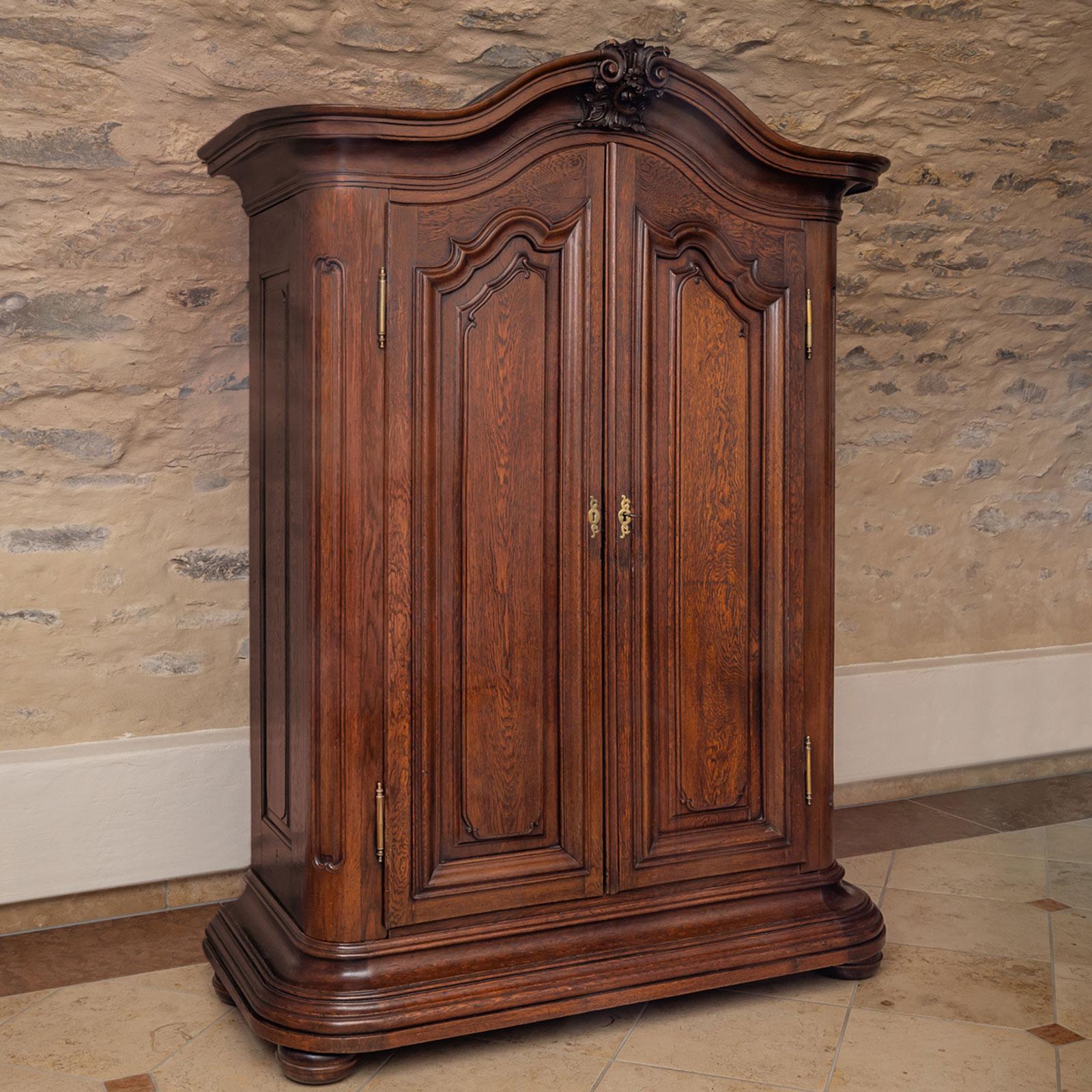 Un grande armadio barocco a due ante realizzato in rovere massiccio nel XVIII secolo. L'armadio è caratterizzato da una zona di base fortemente profilata e da ante con pannelli dal design intricato, mentre le sezioni superiori hanno uno stile