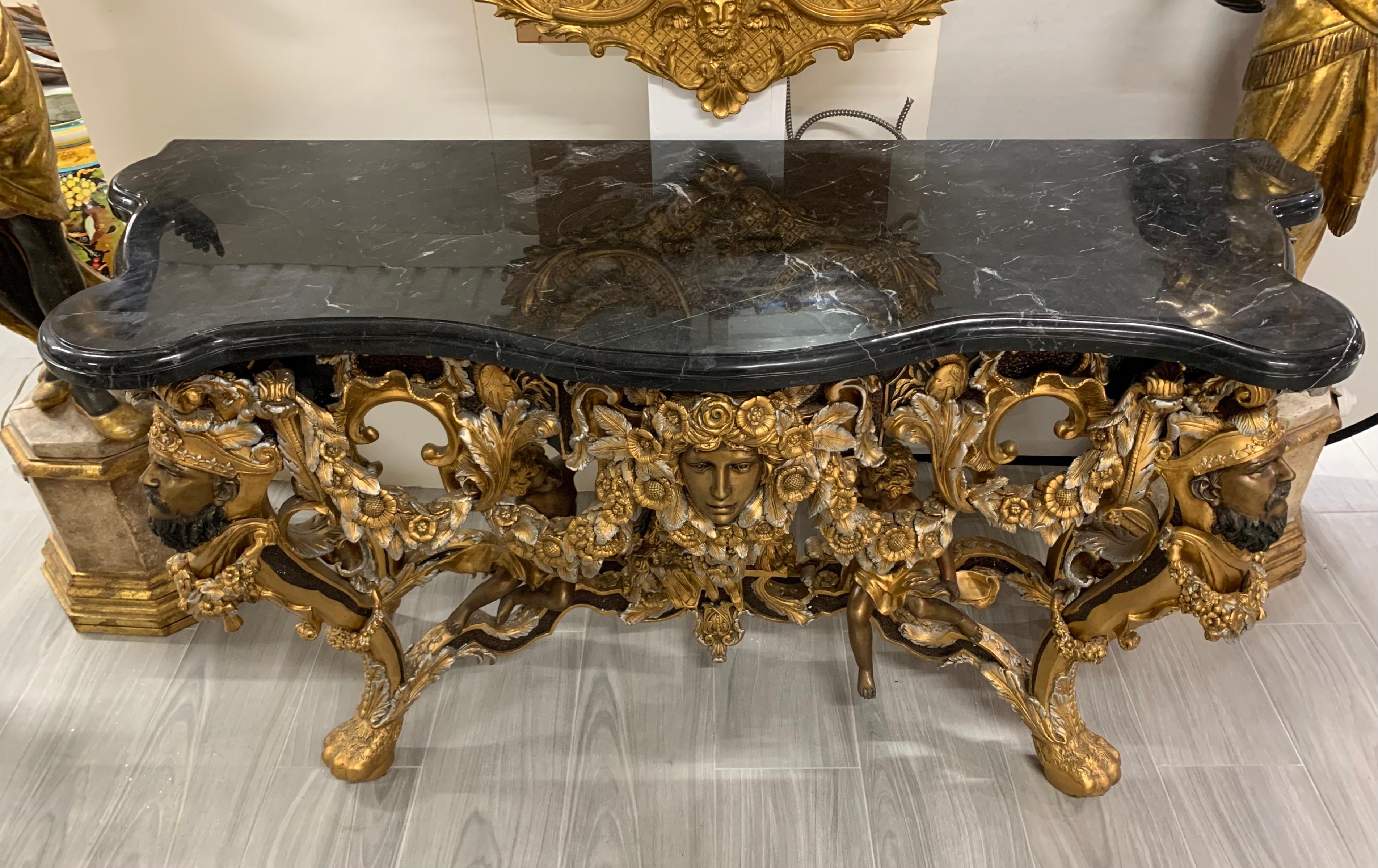 Exuberantly carved bronze console table features a detailed woman’s face in center and faces of soldiers on the four corners. The bottom stretcher has carved cherubs flaunting a soldier’s shield and armor. Intricate carved floral sprays cover the