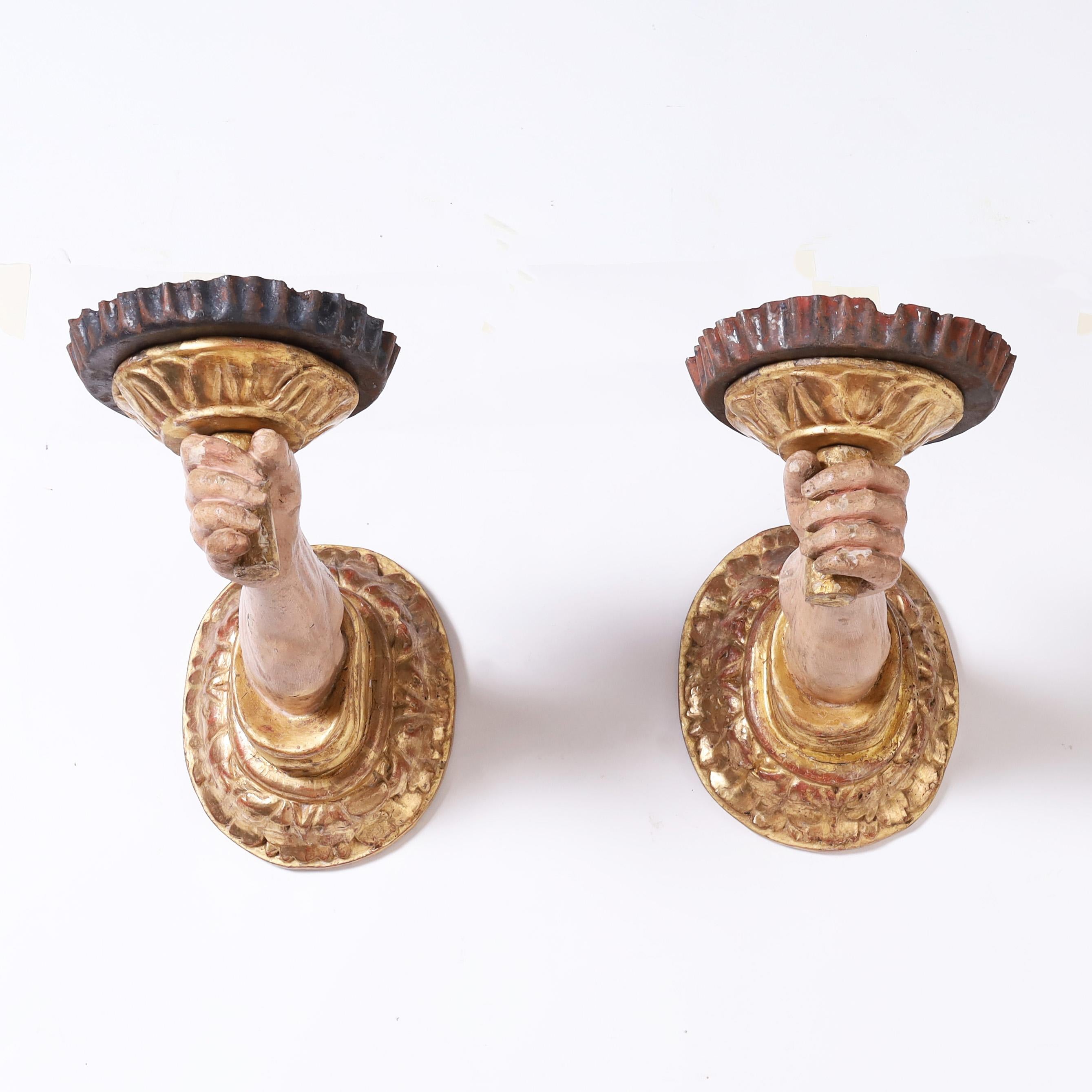 Rare and remarkable pair of 18th century French wall sconce candle holders hand carved depicting hardworking peasant hands in service, protruding from carved, primed and gilt classical back plates, and holding carved wood and metal candle cups.