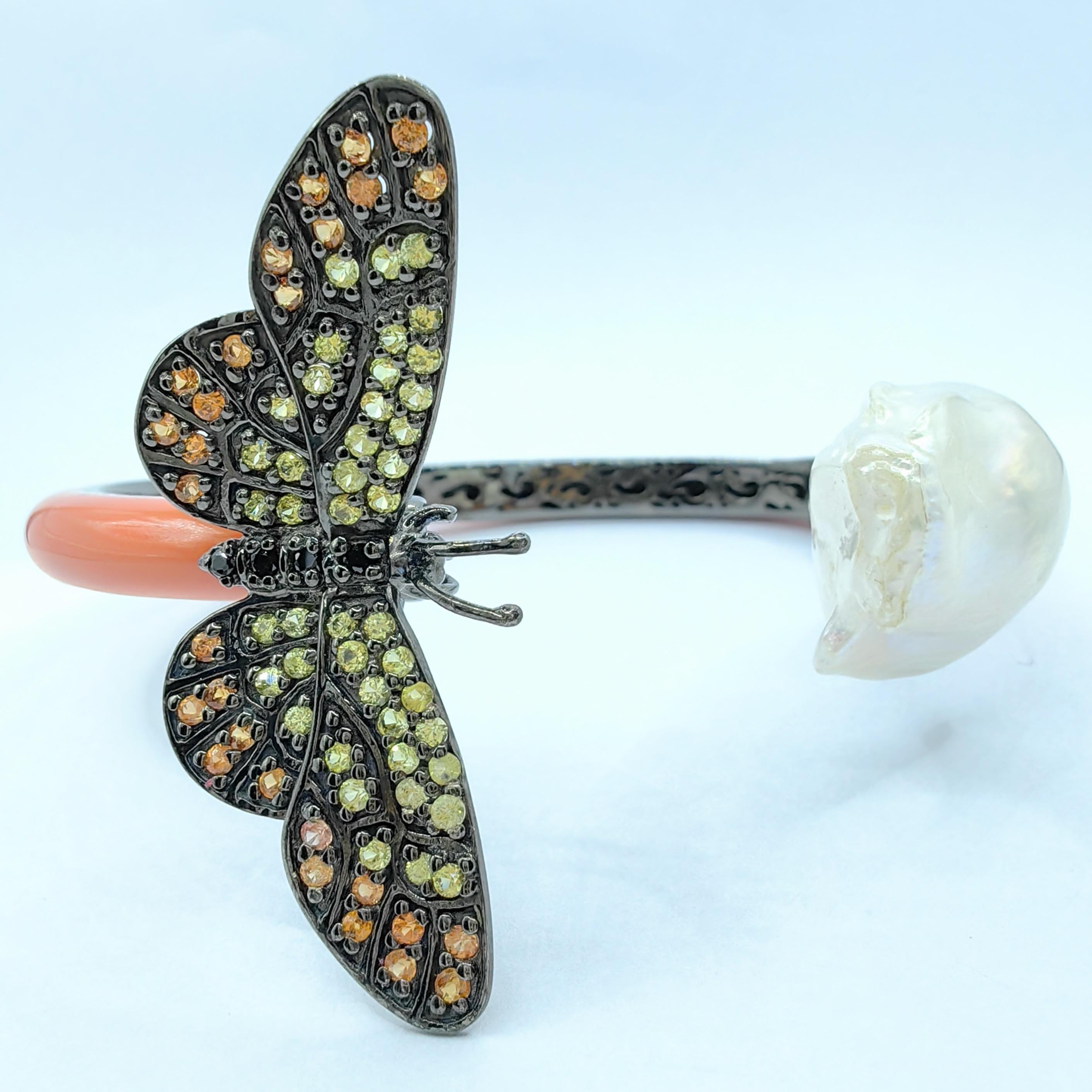 The Baroque Pearl and Sapphire Butterfly Orange Cuff Bracelet in Sterling Silver is a captivating piece that blends elegance with playful charm. At one end of the cuff, a freshwater Baroque pearl showcases its natural, one-of-a-kind shape, with a