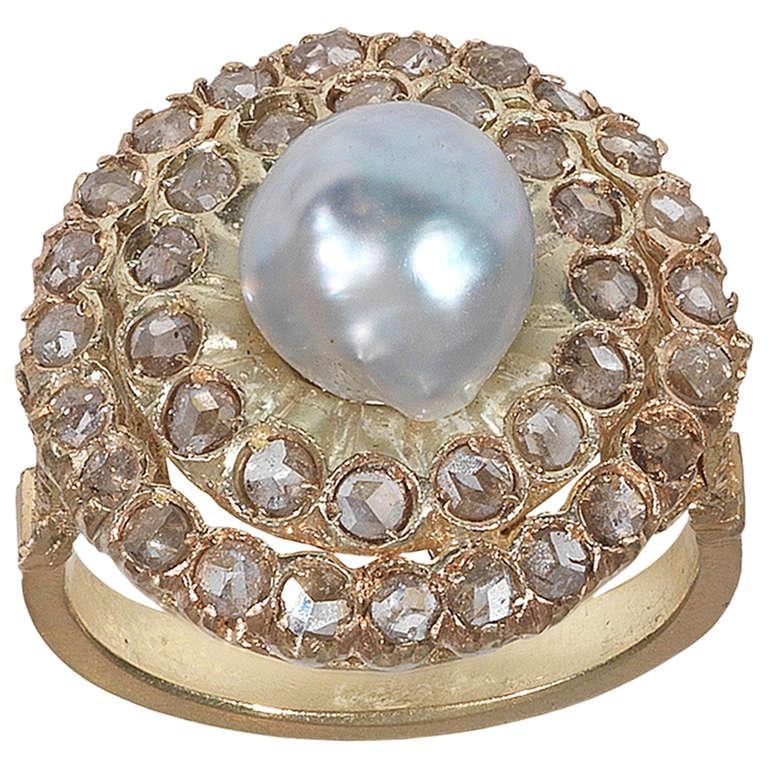 
The central baroque pearl to a rose-cut diamond cluster surround, the carved and engraved gallery to a foliate trifucated shoulders and plain hoop. Mounted in yellow gold.

Weight: 7.8 gr

Finger size: 7