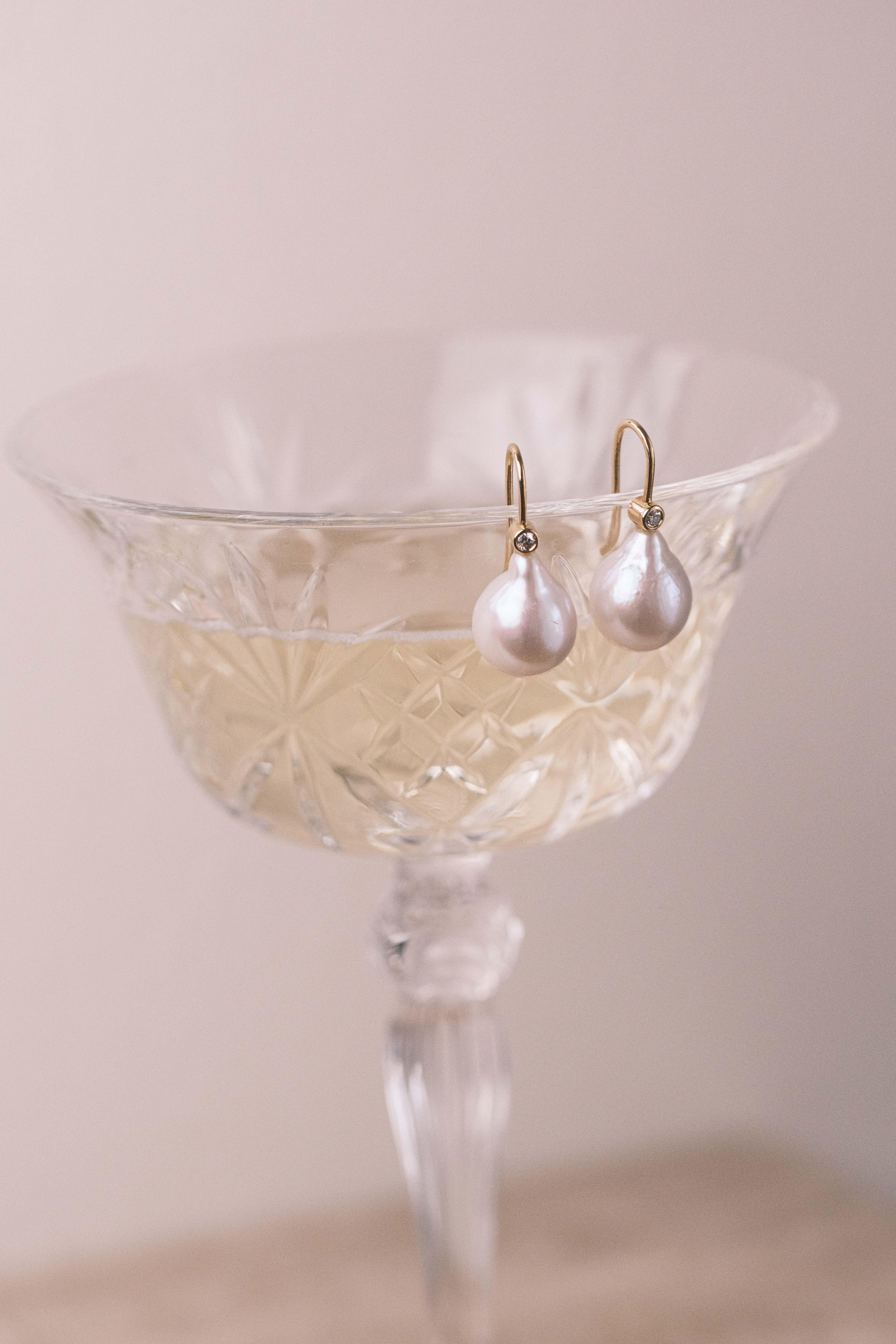 These stunning Michelle Massoura earrings feature baroque drop shaped pearls and glimmering bezel set natural diamonds. Their slim hook design ensures they are easy to slip on and comfortable to wear. Due to the organic nature of the pearls every