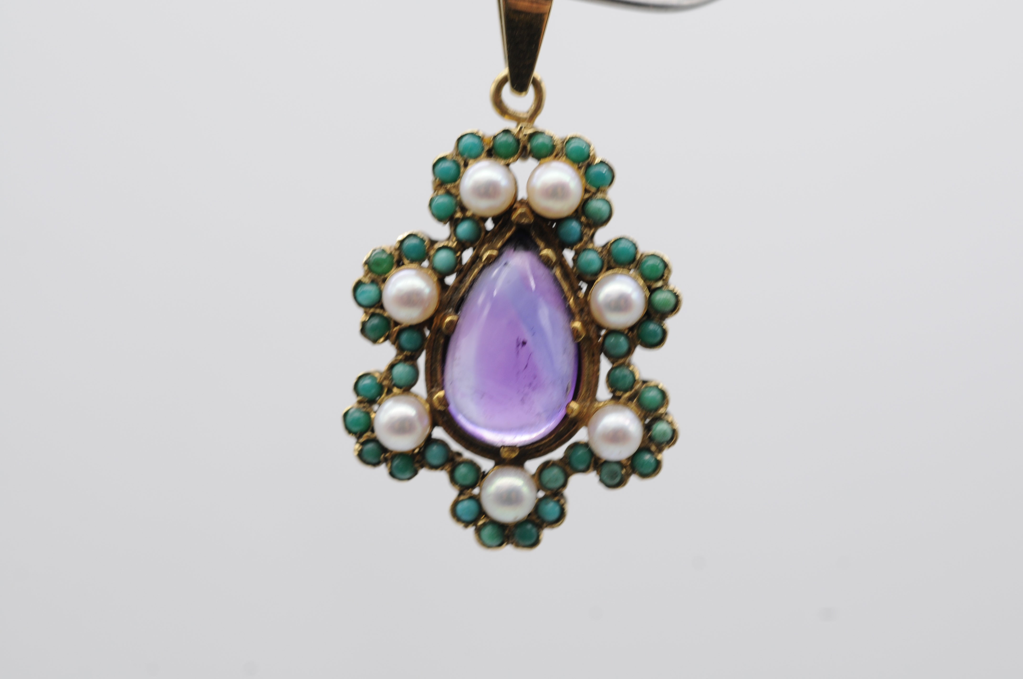 Questo squisito ciondolo antico in oro giallo 14k mette in mostra uno splendido pezzo centrale: una grande ametista cabochon a forma di pera, del peso di circa 5 carati. La ricca tonalità viola dell'ametista è splendidamente completata da una serie