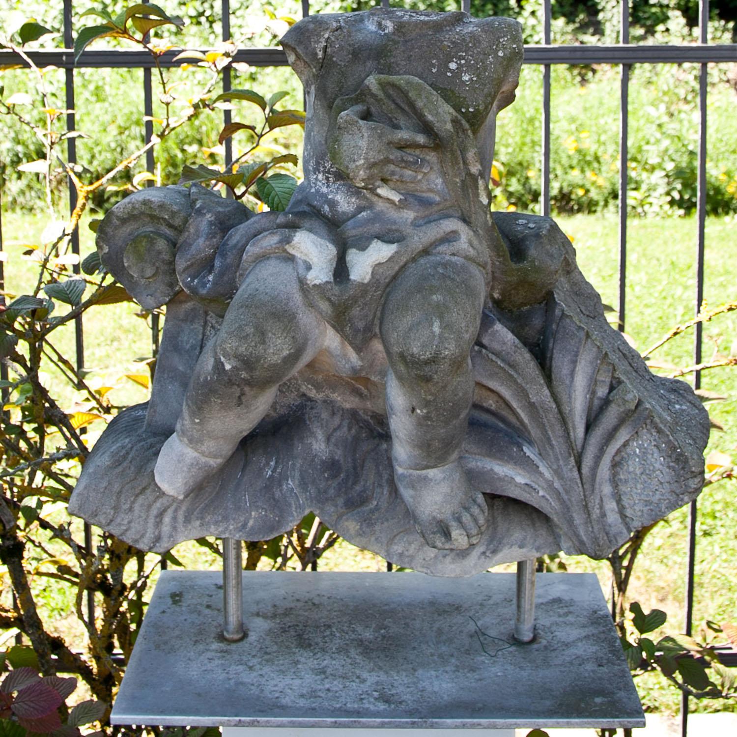 Baroque sandstone fragment of a putto sitting on a rocaille ornament with waves and leaves. The head, arms and parts of the ornament are missing. Very beautiful and naturally aged patina. The sculpture is mounted on a metal frame.