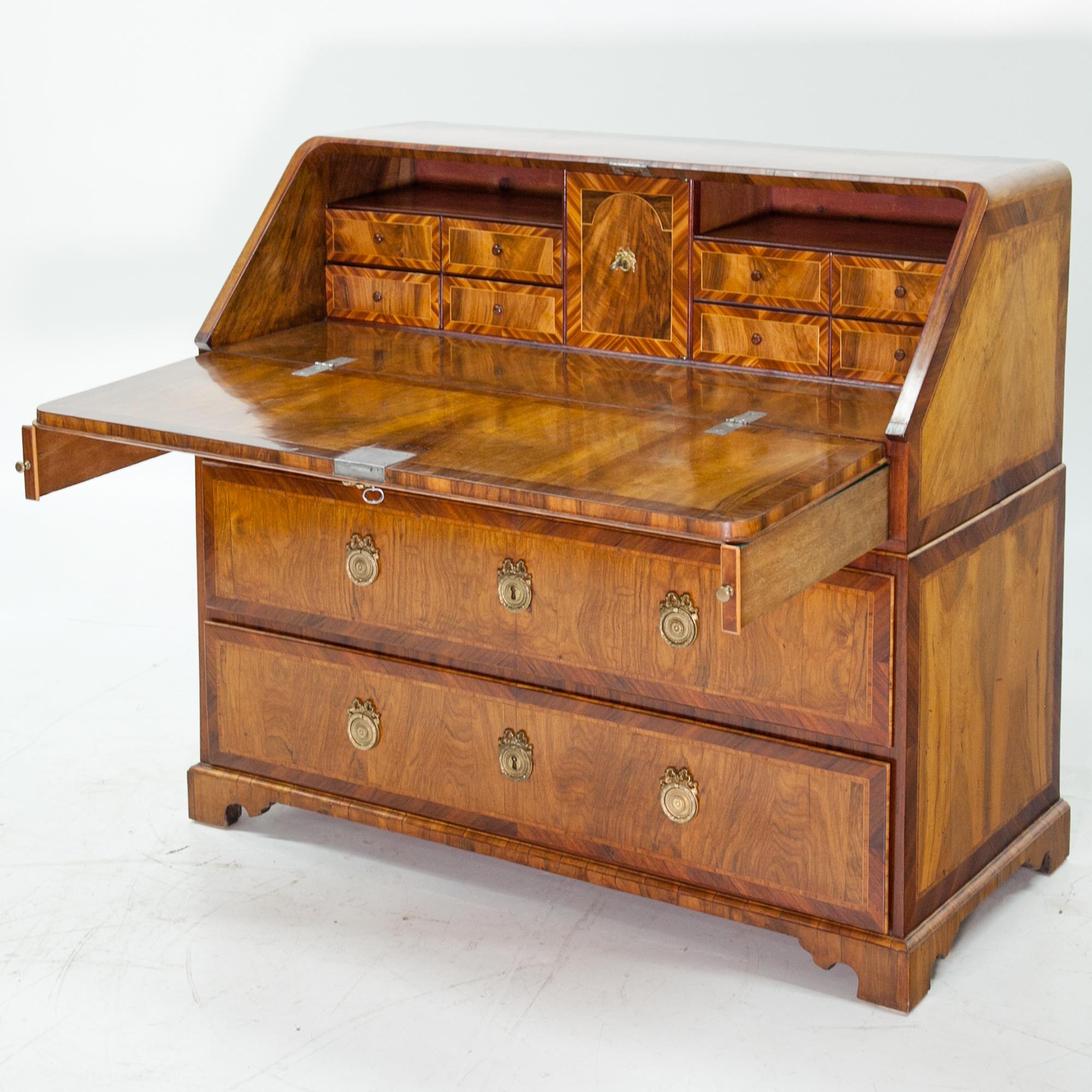 Baroque secretaire on a carved base with four drawers and a hinged writing surface. The sides and the front shows filling-shaped veneer work. The top has rounded corners and the interior consist of eight small drawers and a central tabernacle