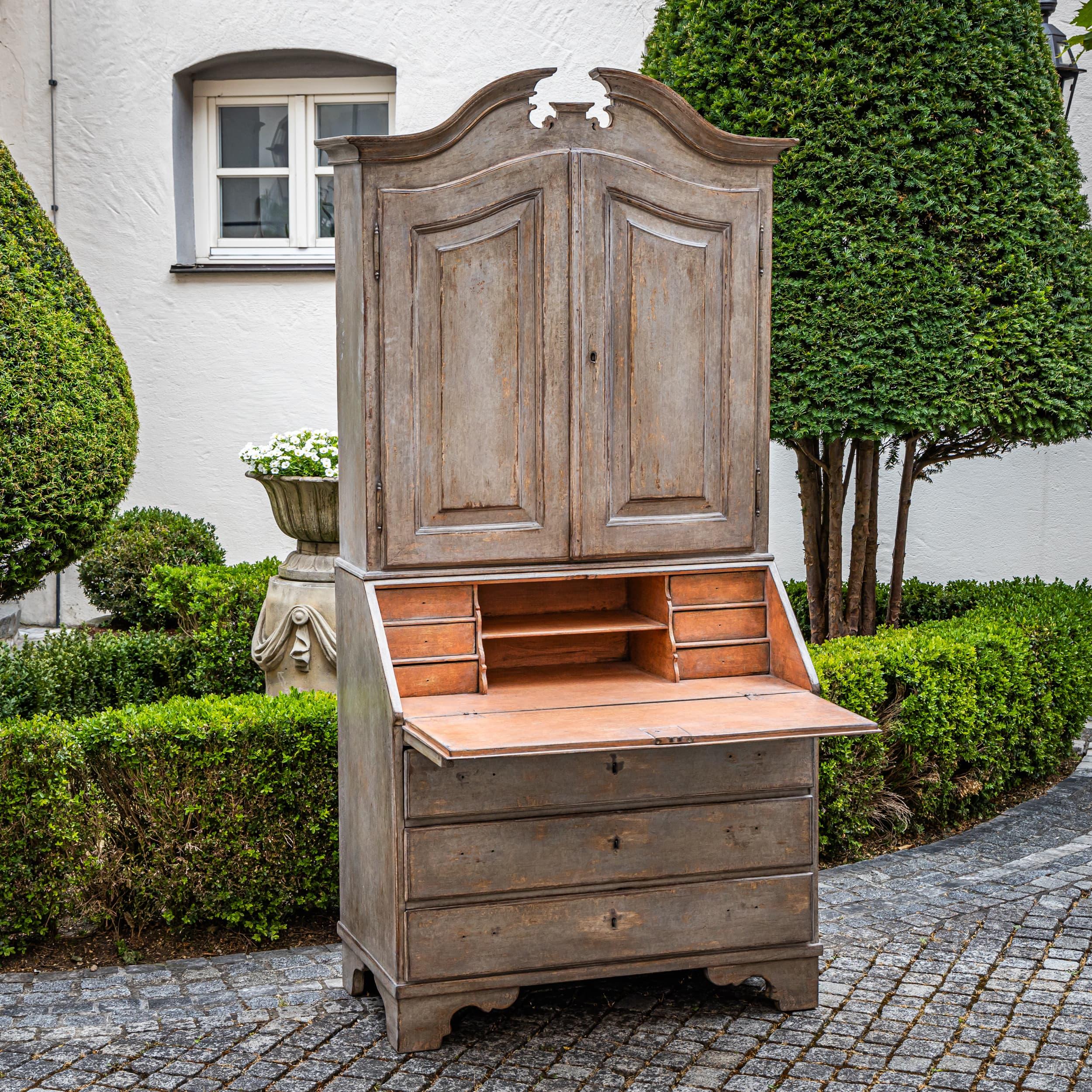 Handbemalter Barocksekretär mit dreischübigem Kommodensockel, schräger Schreibklappe und zweitürigem Schrankaufsatz, der von einem gebrochenen Giebel gekrönt wird. Die Lackierung - außen hellgrau und innen ziegelrot - wurde neu aufgetragen und