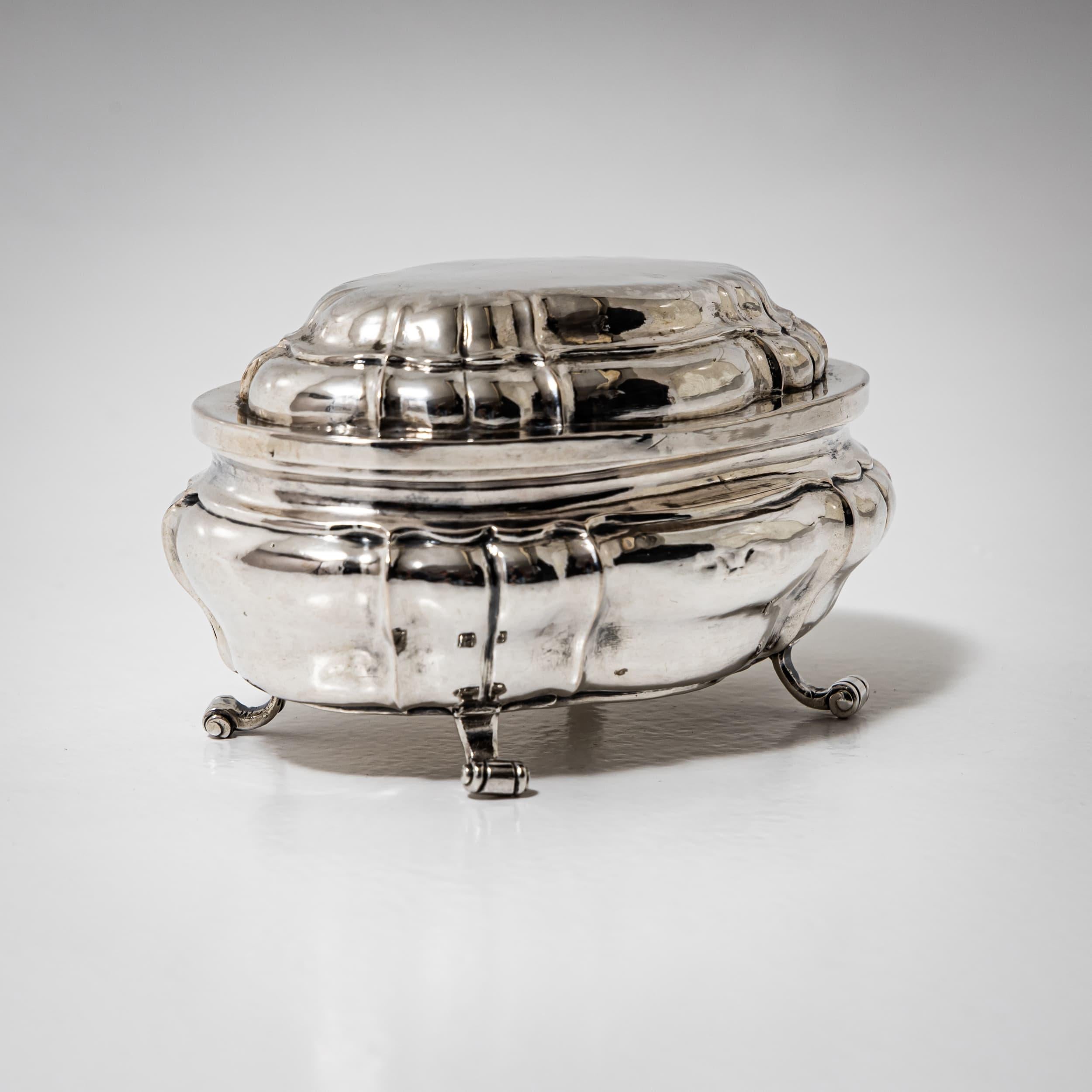 Piccola scatola barocca con coperchio in argento, finemente lavorata, che poggia su quattro eleganti piedini a voluta. Il corpo presenta lati delicatamente ondulati e un coperchio a cupola. Sulla base è presente il marchio della città di Coblenza e