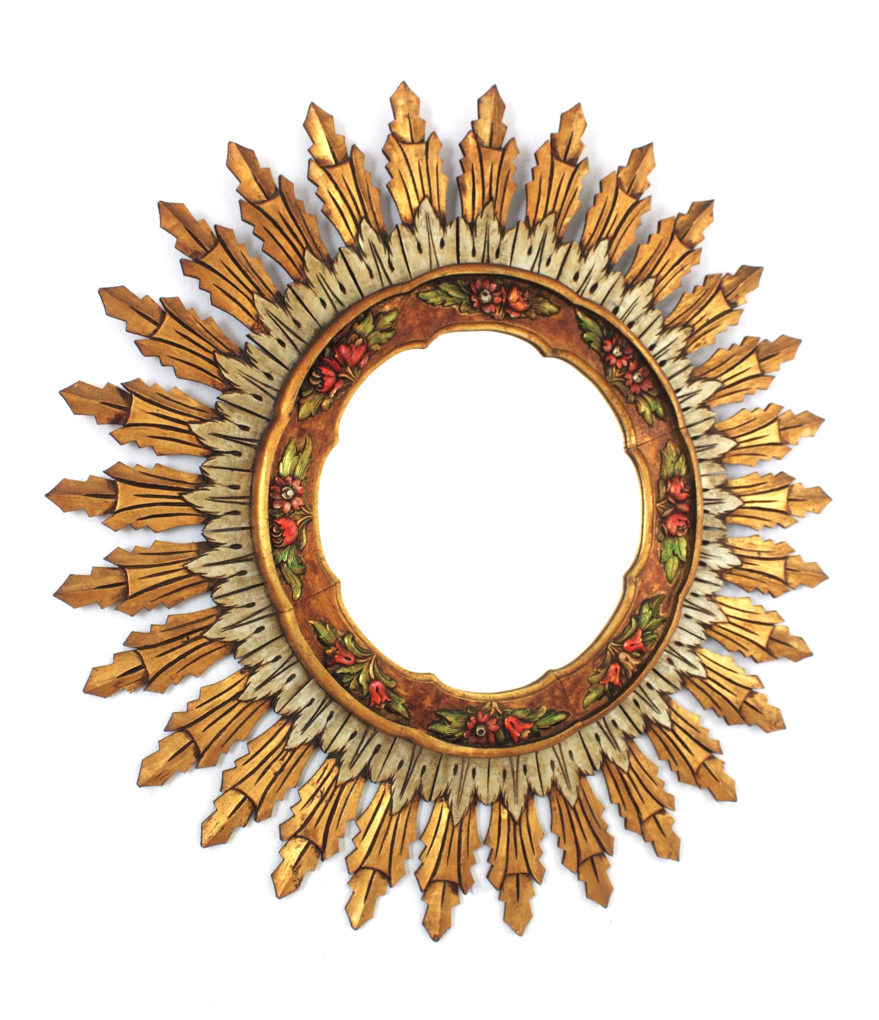 Spanish Carved Gilt and Silvered Wood Sunburst Mirror
Double Layered Giltwood Sunburst Mirror with Carved Polychrome Floral Details. Spain, 1960s.
This wall mirror features a layer of long rays at the back part and a layer of silvered shorter ones