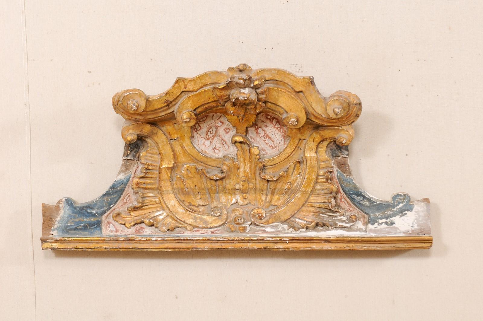 An Italian 19th century carved-wood wall hanging pediment fragment. This Italian Baroque style pediment, from the early 19th century, has gilt over gesso and wood, hand-carved in a volute and acanthus leaf motif with flower at crest, and faux