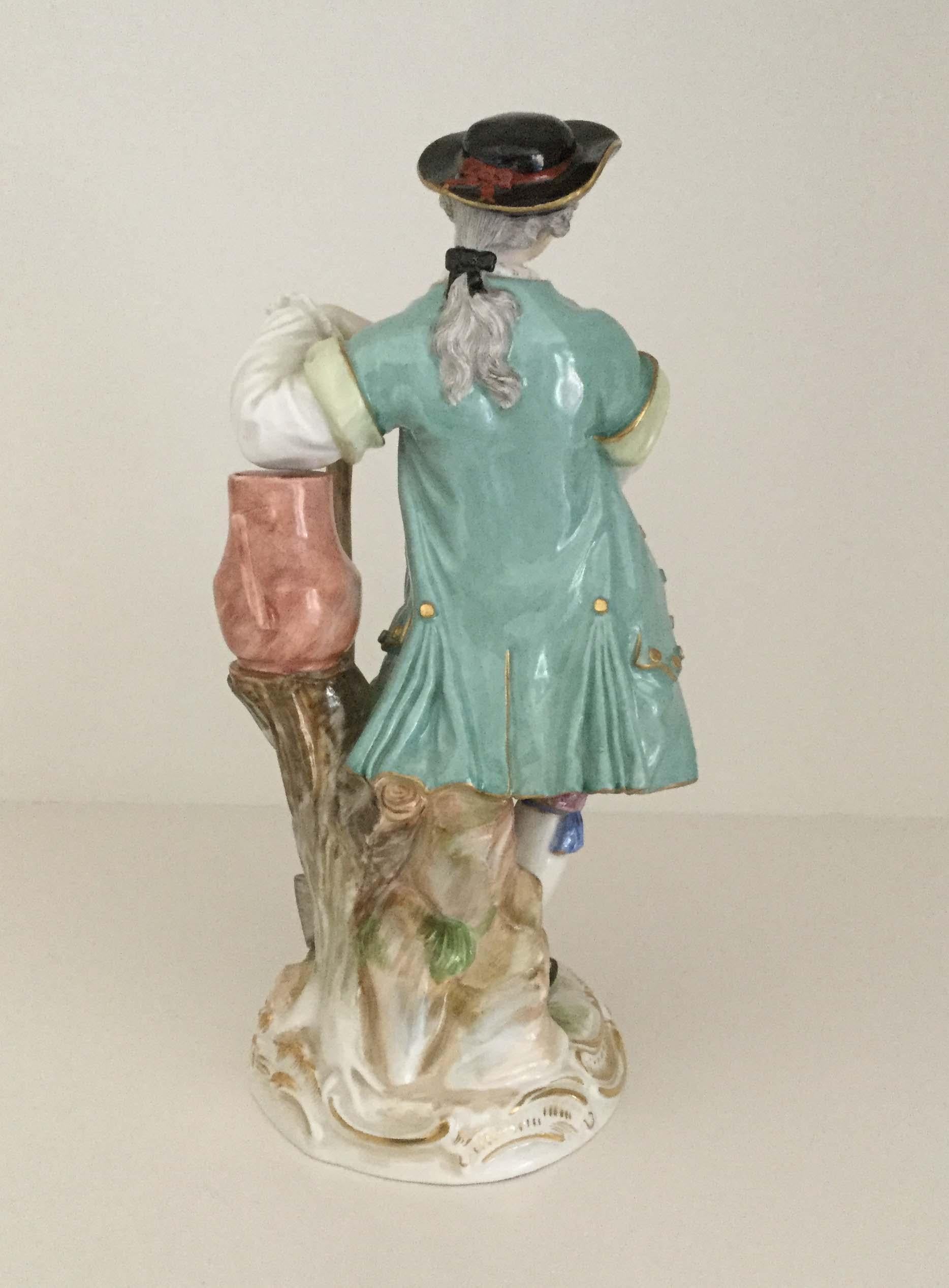 A late 19th century Meissen figurine of a gardener in Baroque style, dressed in a black and gilt rimmed hat, a flared green jacket over a waistcoat with gilt highlights and breeches with pink and blue decoration, white stockings and black buckled
