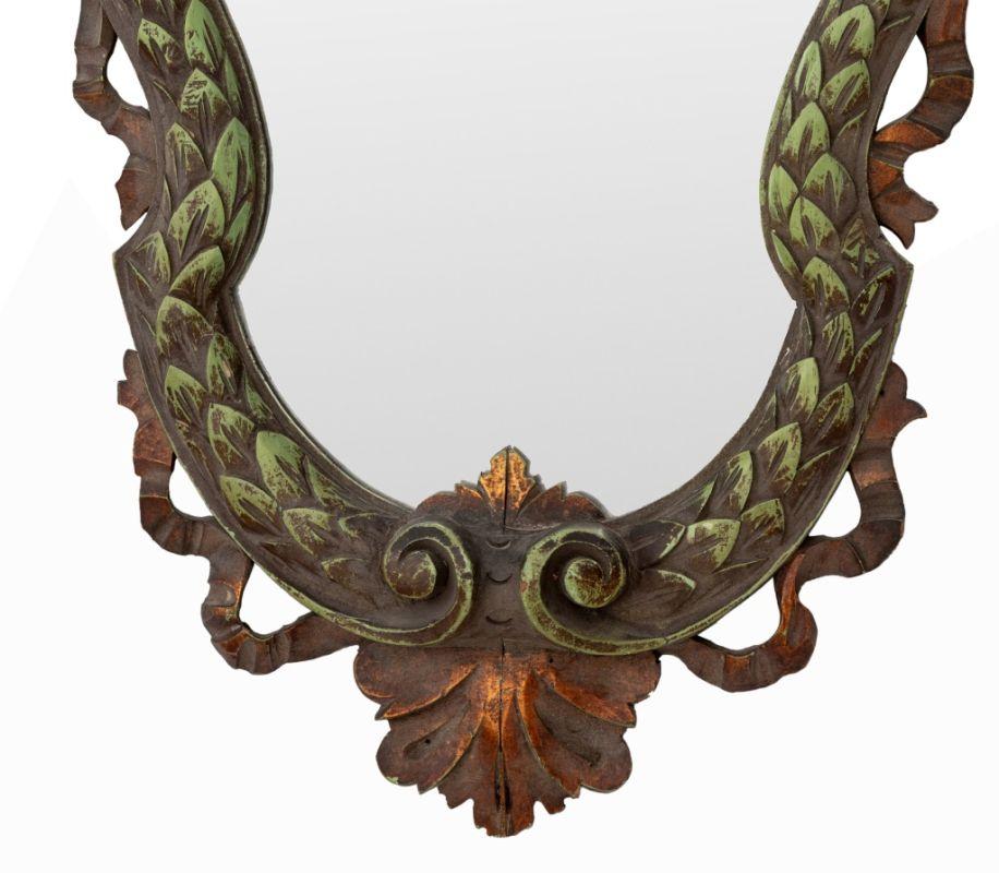 Baroque style paint-decorated and carved wood wall mirror. The mirror is a shield form with a foliate and serpentine motif. 