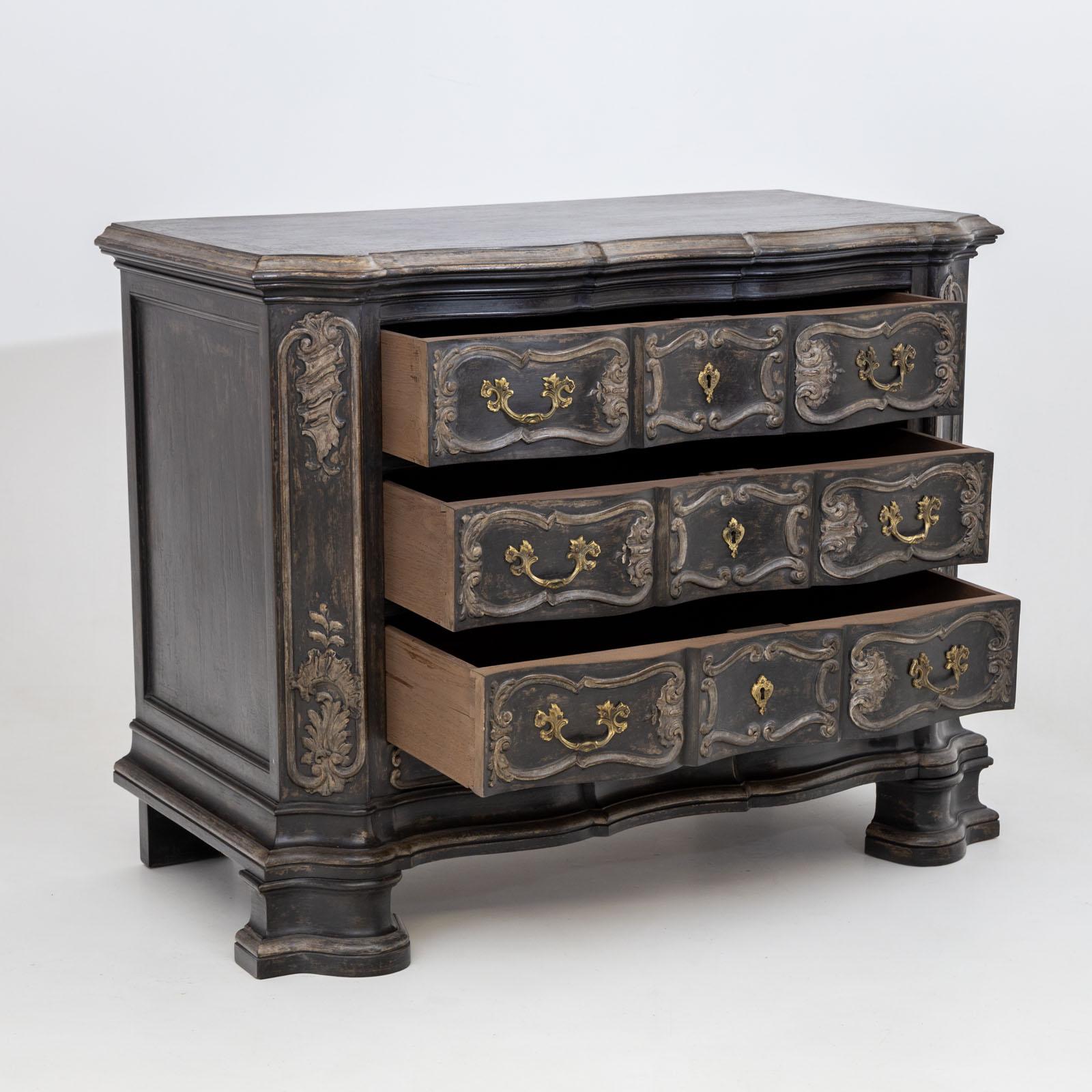 Large Baroque-style chest of drawers with three drawers and a curved front. The chest of drawers stands on wide profiled feet and is decorated with carved panelled decorations. The black and anthracite grey finish is new and has been given an