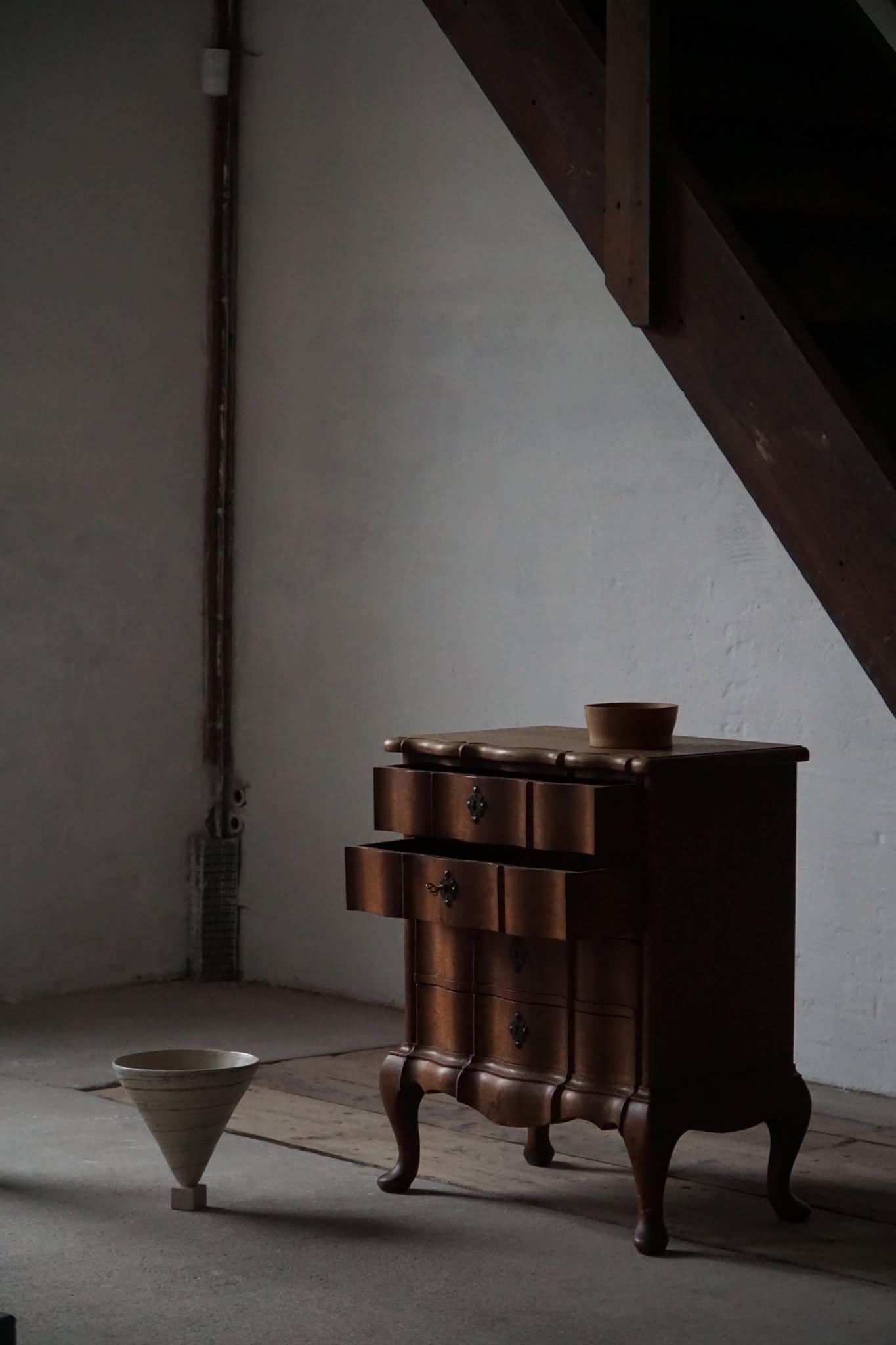 Bellissima cassettiera in stile barocco, realizzata all'inizio del XX secolo. Il pezzo presenta eleganti frontali dei cassetti a serpentina, gambe a cabriole e scanalature decorative in metallo che evidenziano la sua classica influenza