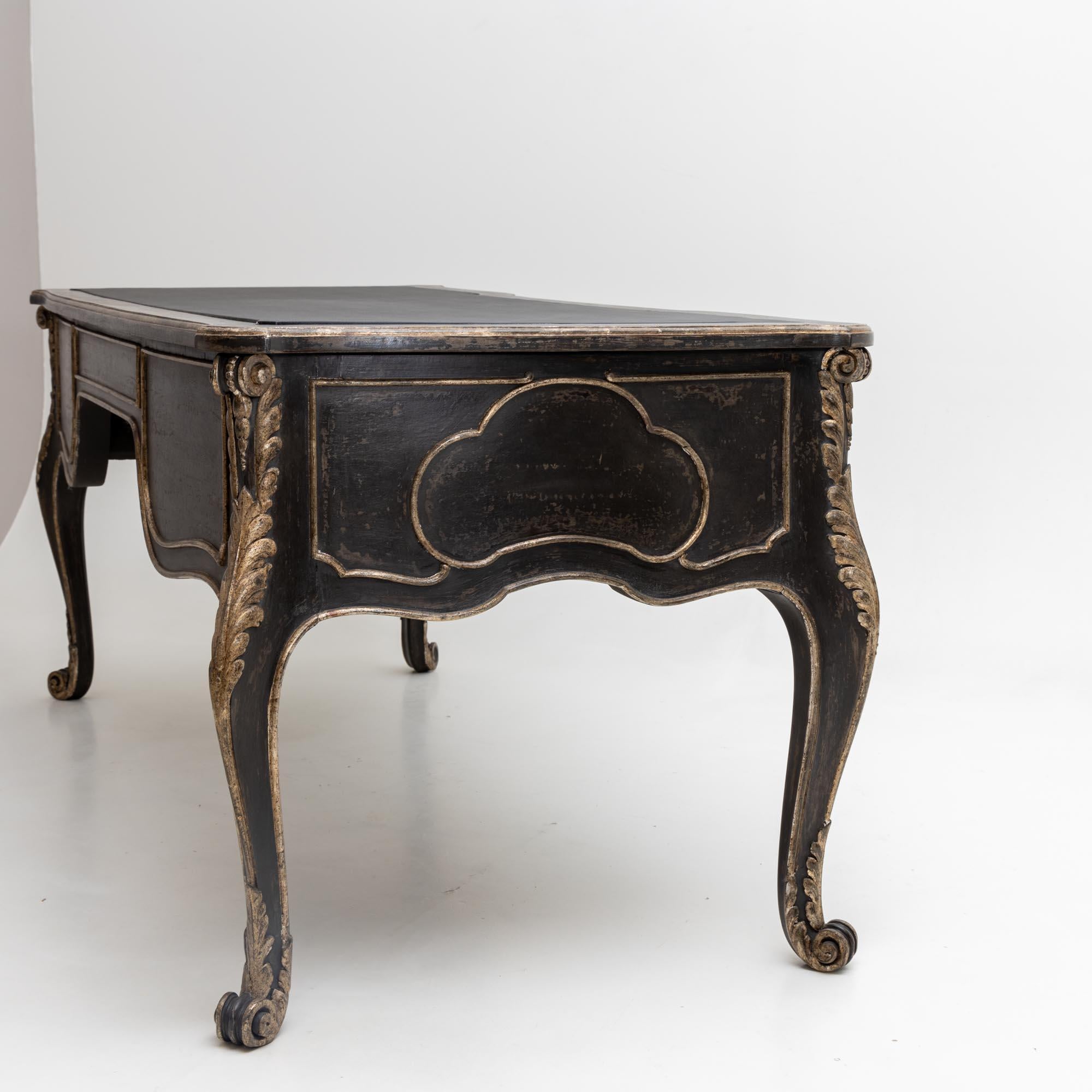 Large desk with volute s-legs and five drawers. The writing surface is covered with black imitation leather. The desk has been newly painted in anthracite grey and the decorations have a golden patina.